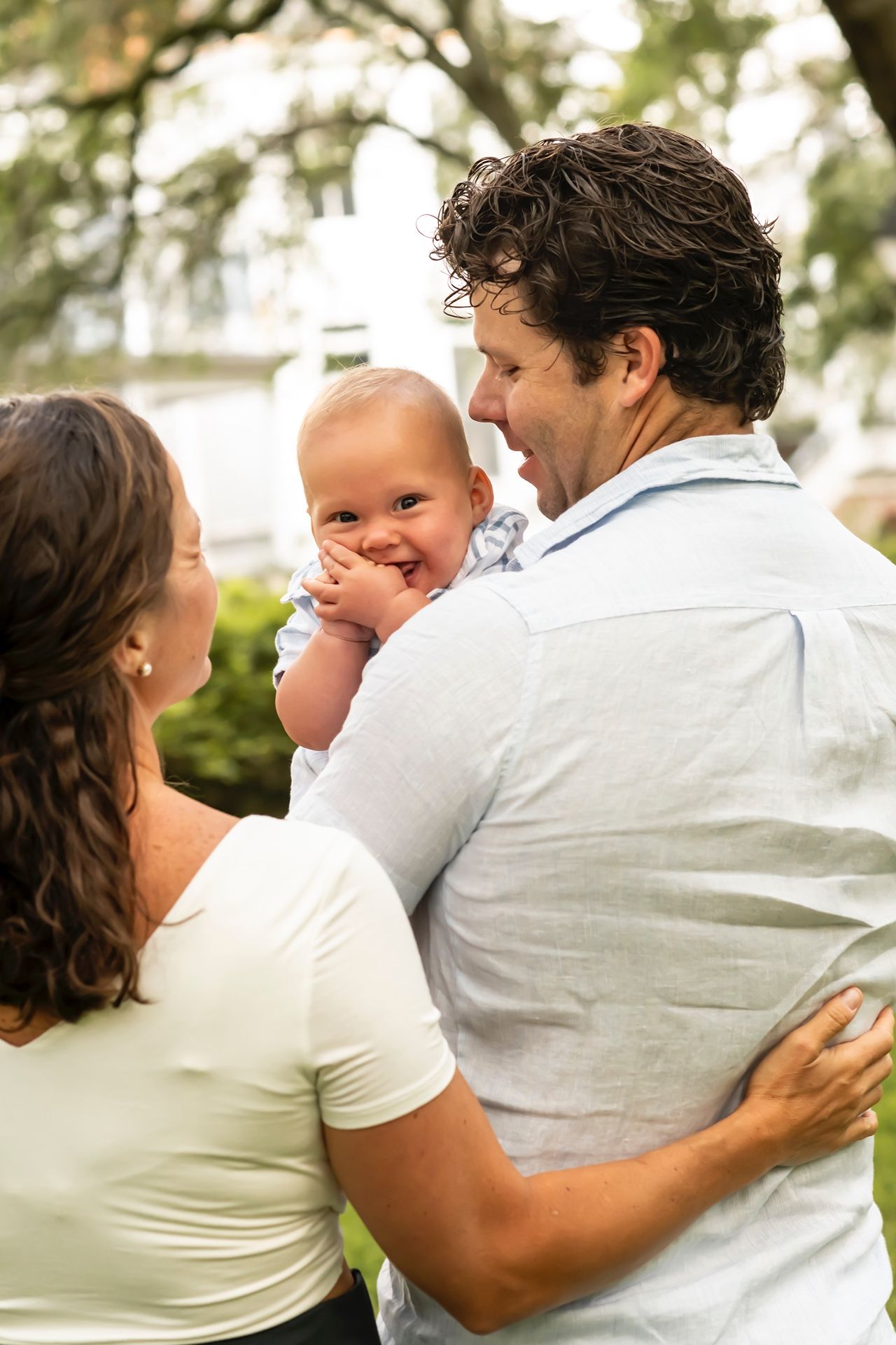 A happy baby laughs while being held between two adults under a canopy of Spanish moss trees.