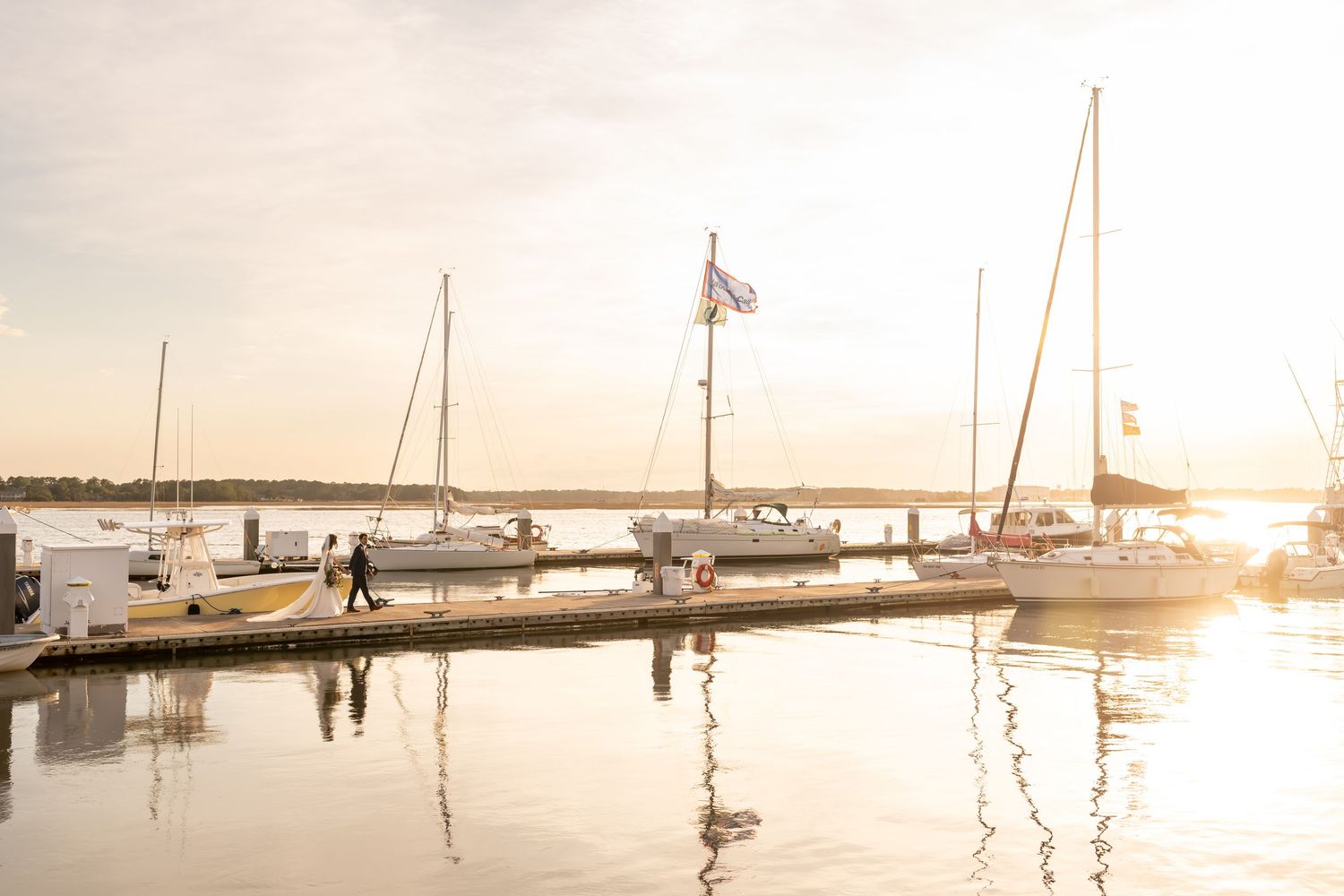 Boats docked at a serene marina during golden sunset with masts reflected in calm water.