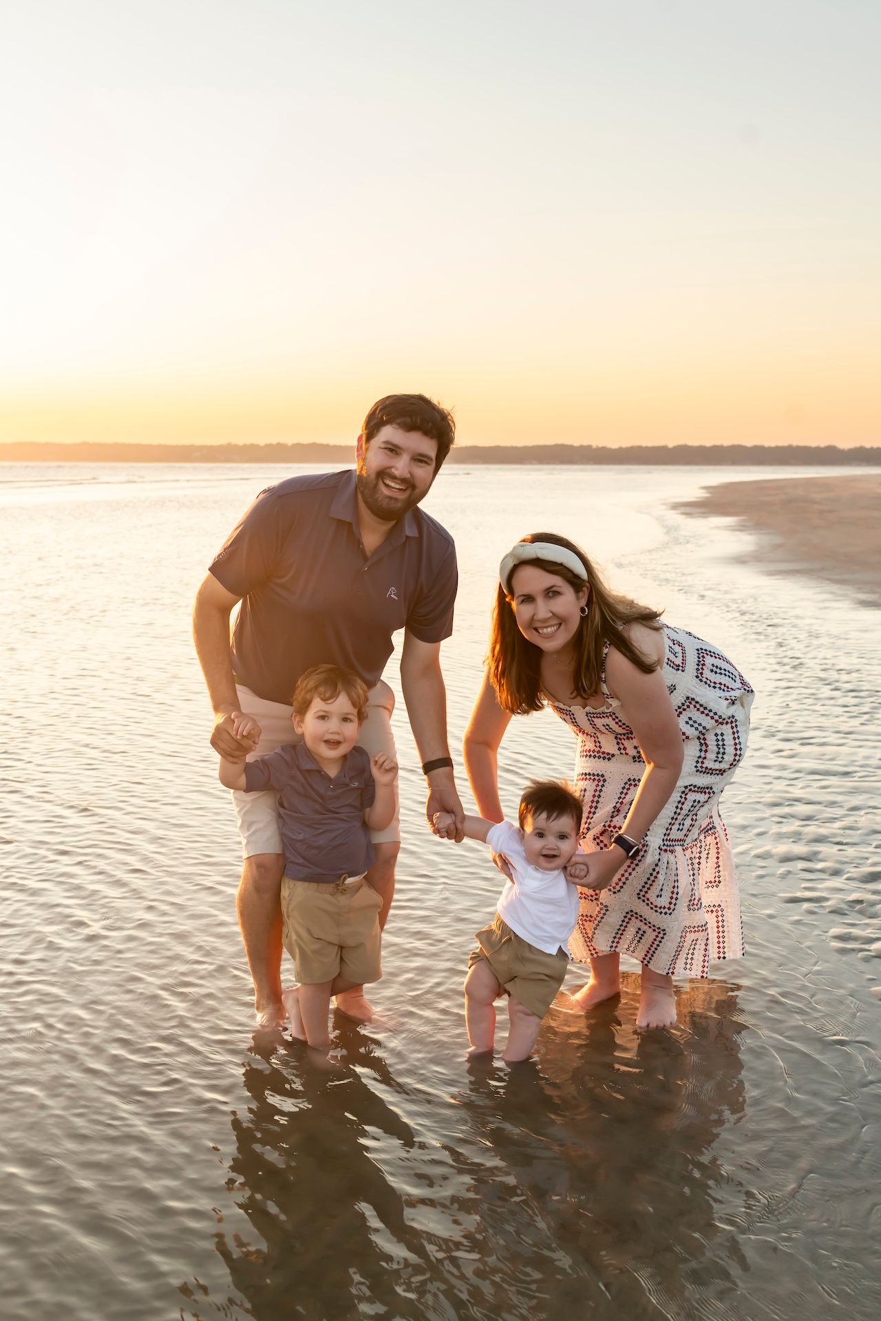 A family splashes and plays together in shallow ocean water during sunset at the beach.