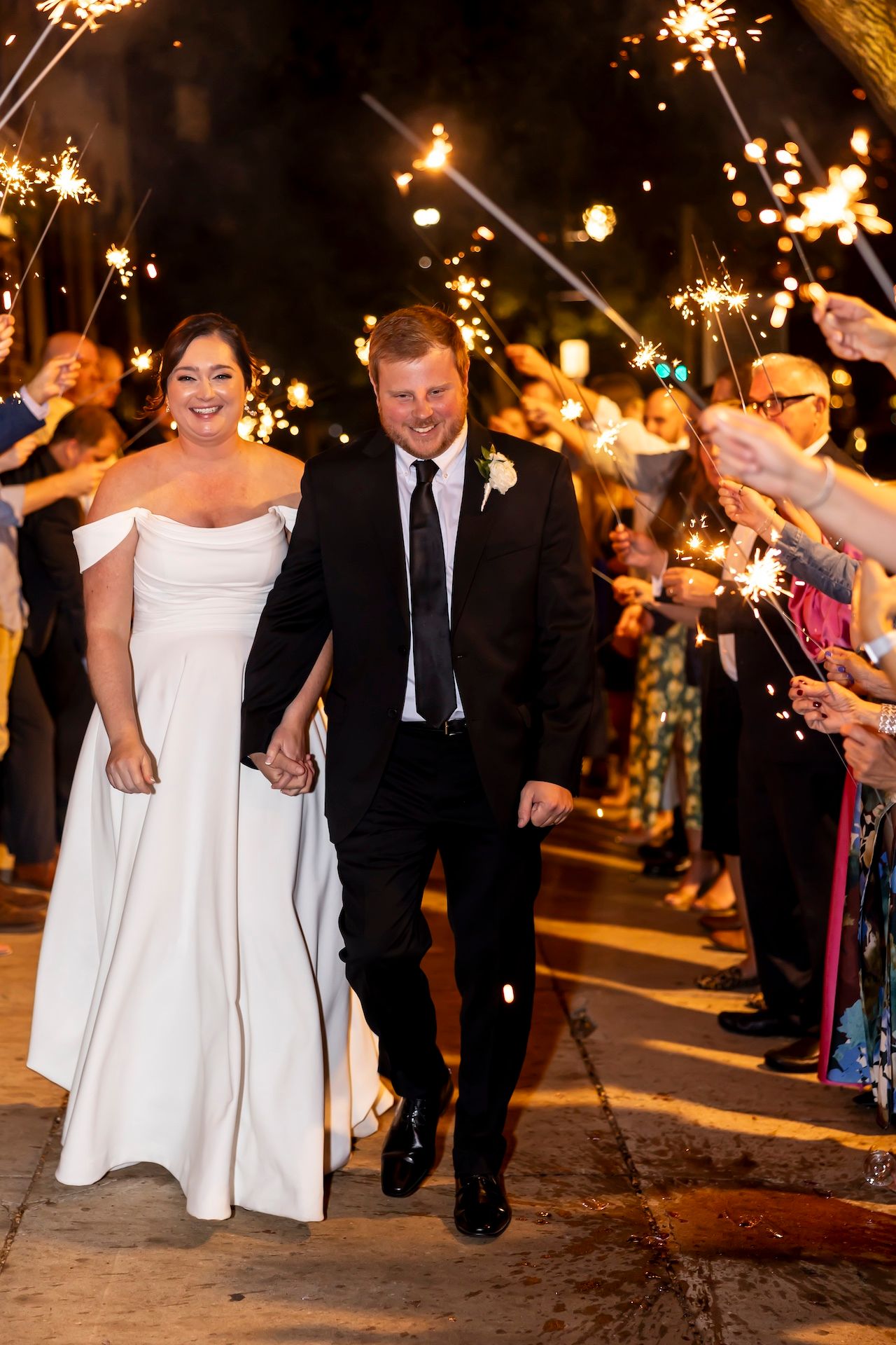 Sparkler exit at a nighttime wedding celebration as couple walks through glowing sparklers held by guests.