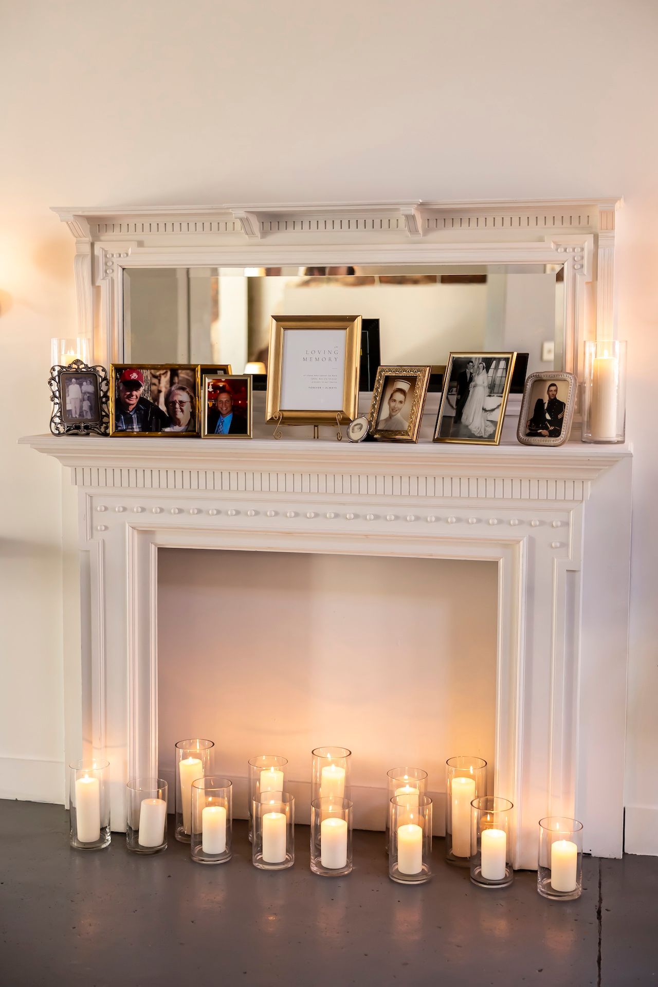 White fireplace mantel decorated with glowing candles and framed family photos for a wedding reception.