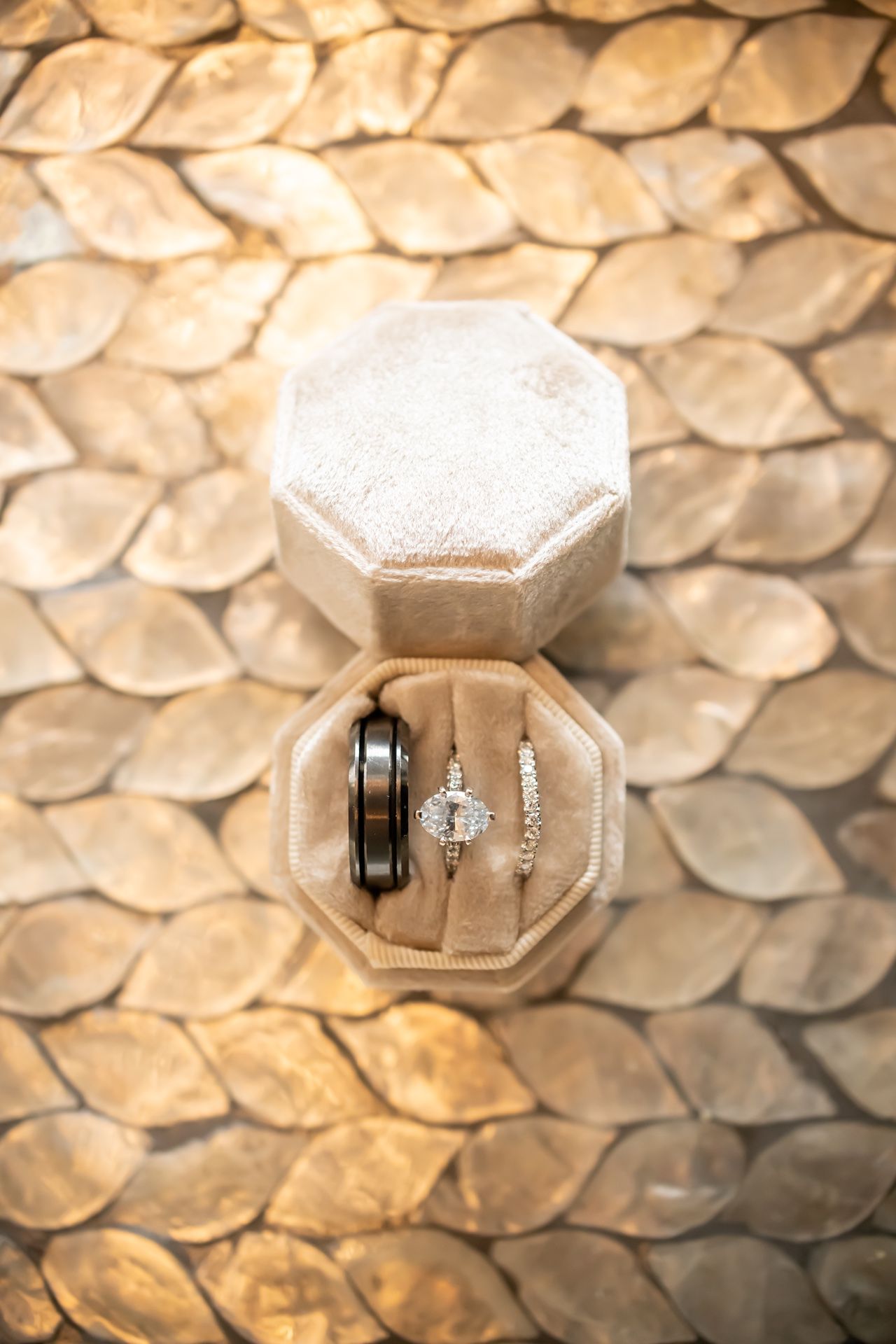 Multiple diamond engagement rings and wedding bands displayed in an octagonal gray velvet ring box against a textured backdrop.