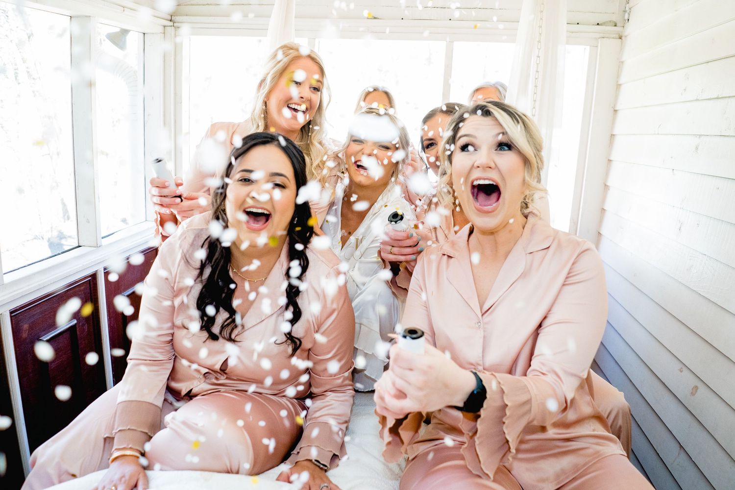 Group in pink pajamas laughing and celebrating with champagne at a festive party gathering.