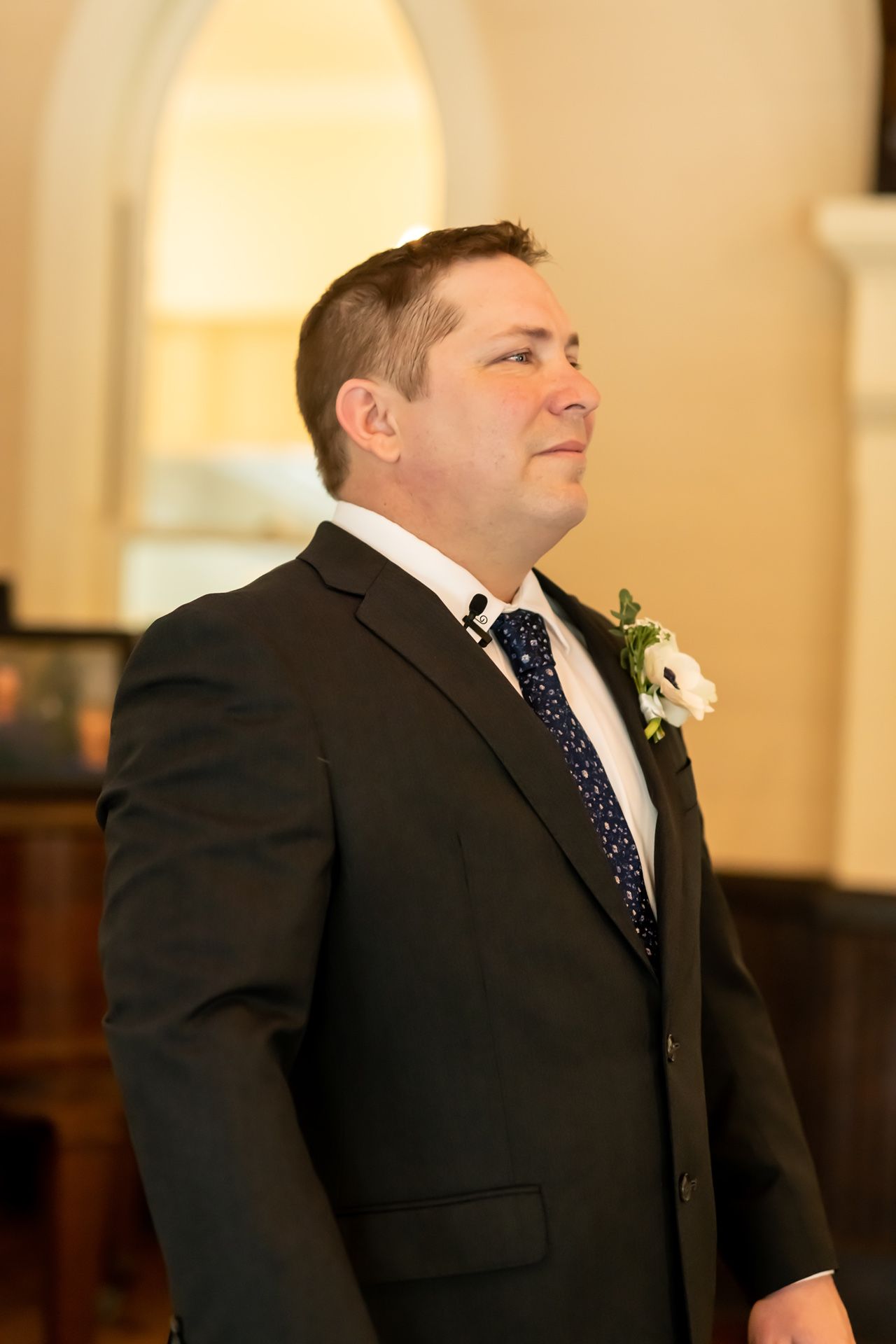 Groom in classic black suit with navy polka dot tie waits during wedding ceremony.