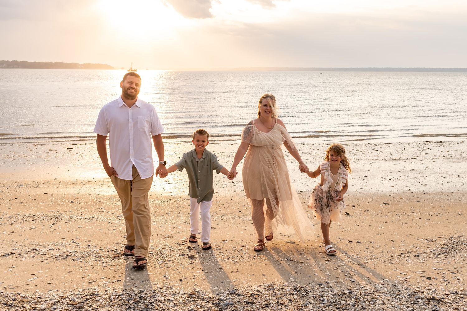 A family group in light colored clothing walking together on a sandy beach at sunset with their shadows visible.