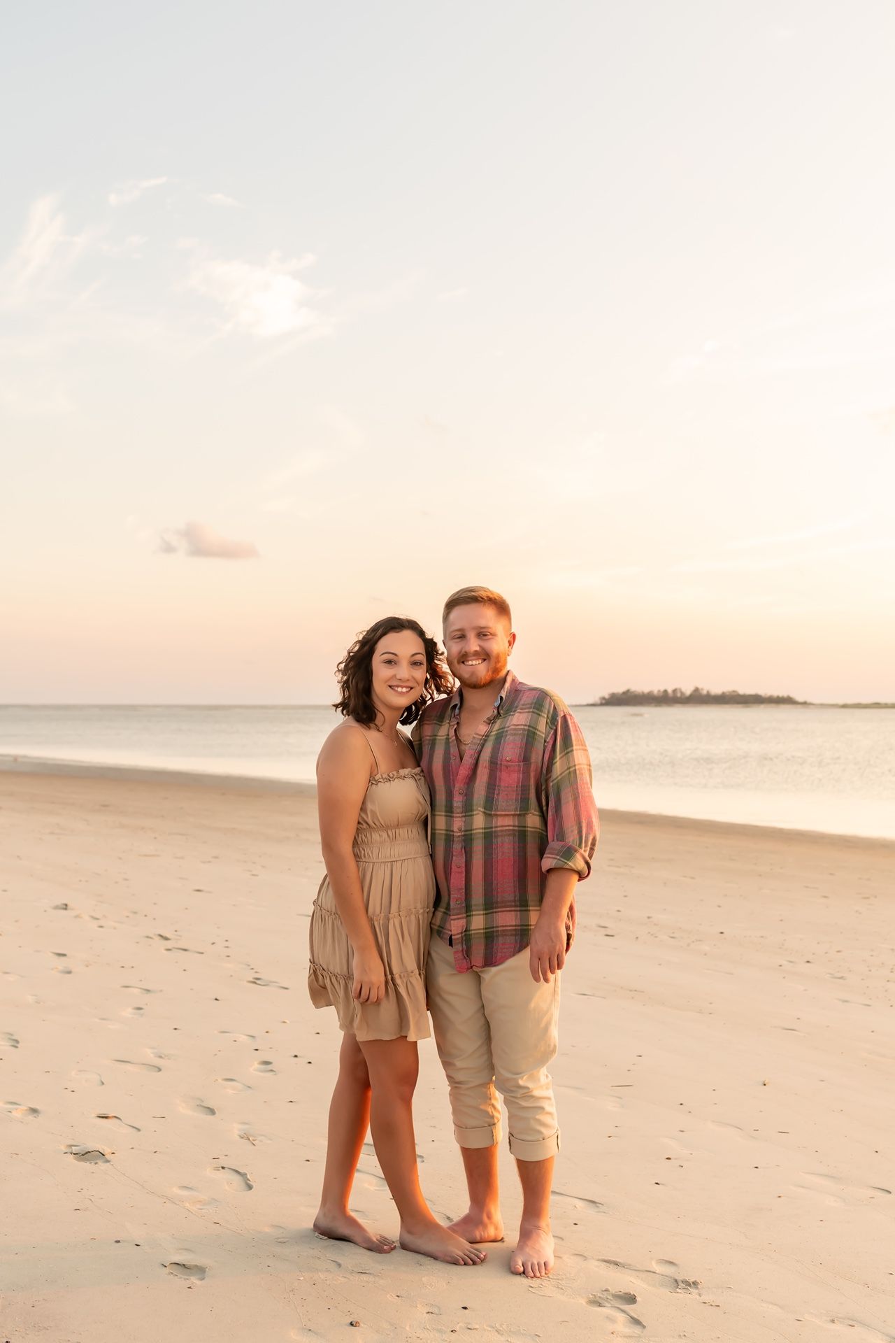 A couple shares a romantic moment on a sandy beach at sunset in warm lighting.