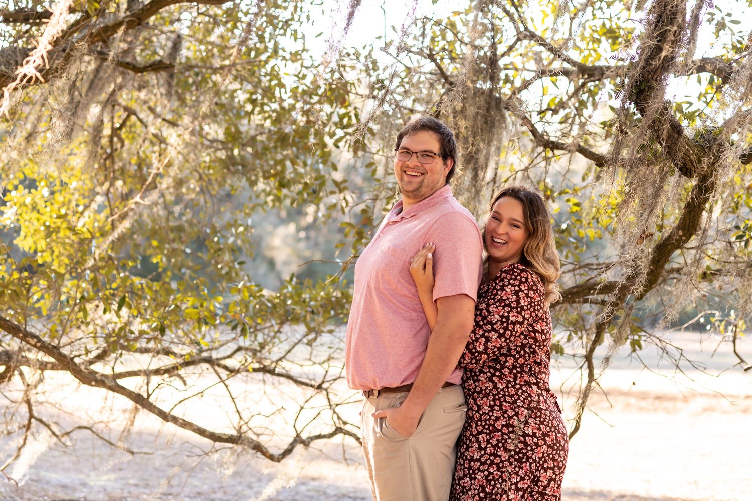 Two people embrace in golden afternoon sunlight with rustic branches and trees creating a romantic outdoor setting.