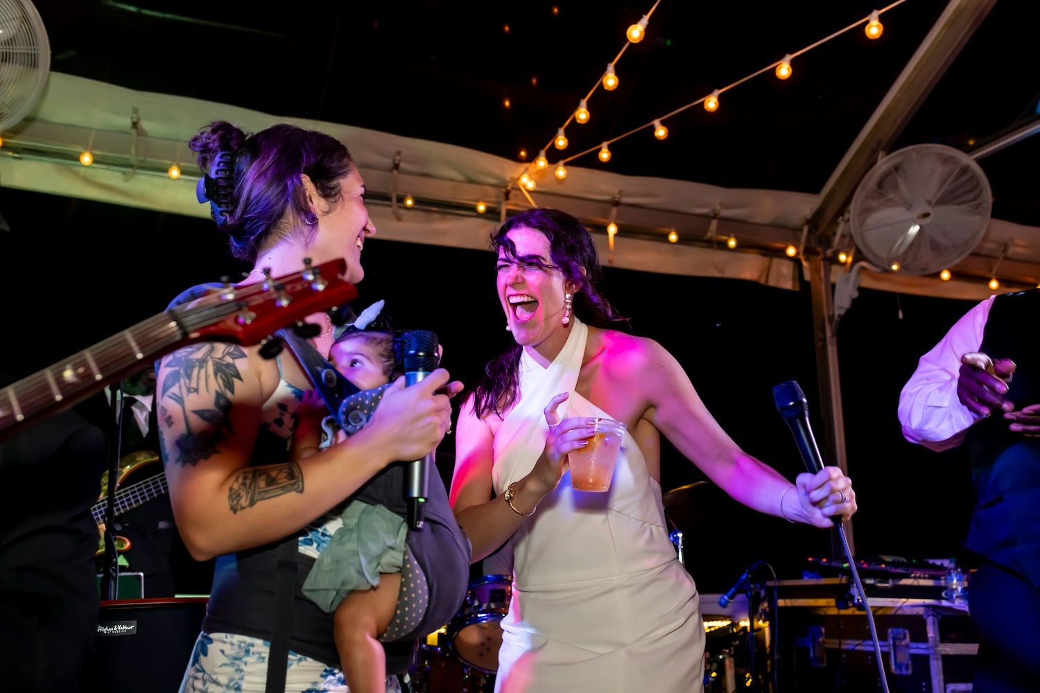 Two people singing and dancing together under string lights at a nighttime wedding reception celebration.
