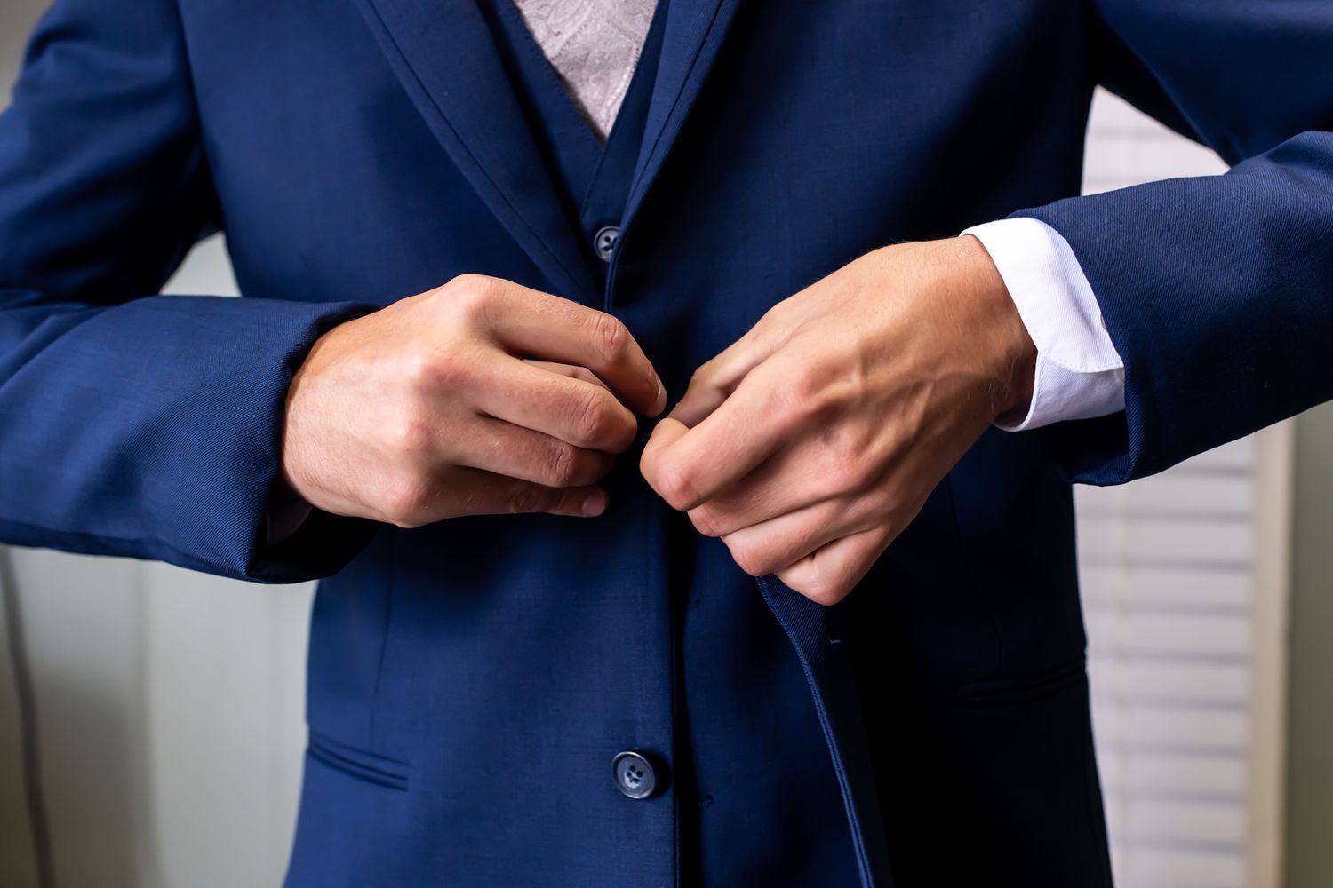 Close-up view of hands adjusting a navy blue business suit jacket button.