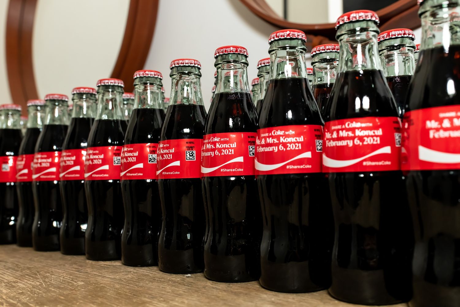 Row of glass Coca-Cola bottles with red labels lined up on a wooden surface.