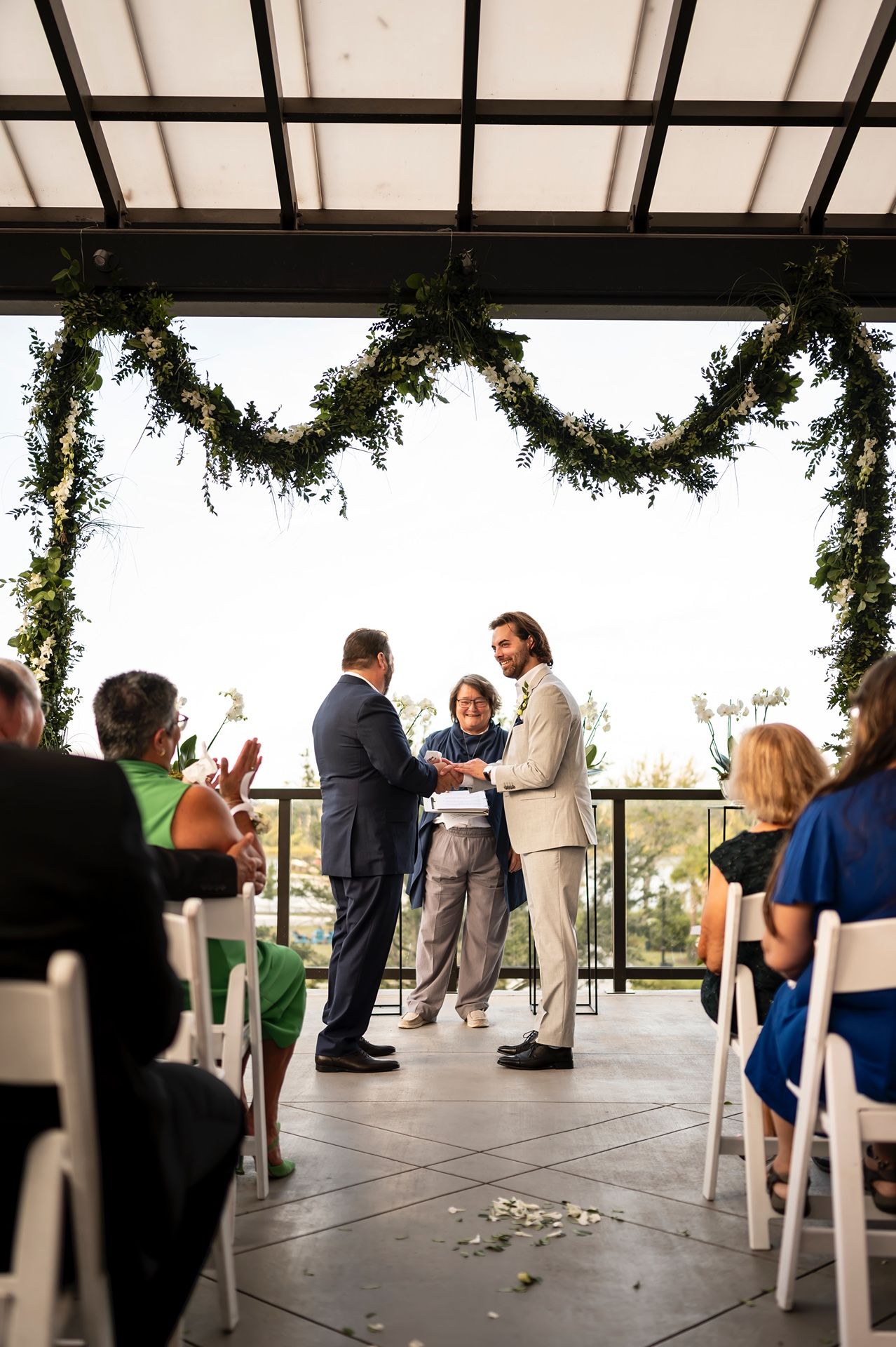 Wedding guests mingling and socializing on an outdoor covered patio decorated with hanging greenery.