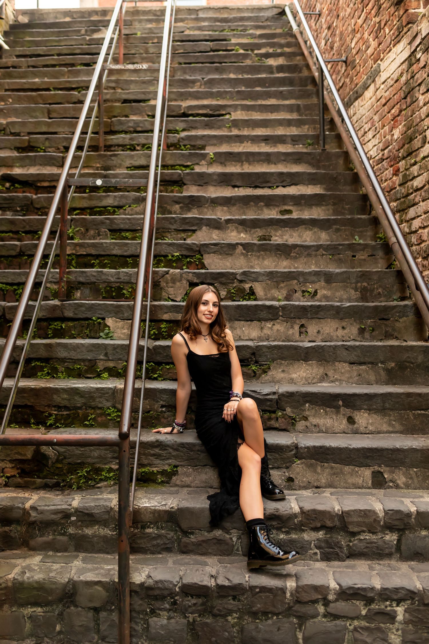 Fashion portrait on vintage brick steps with metal railings in urban setting.