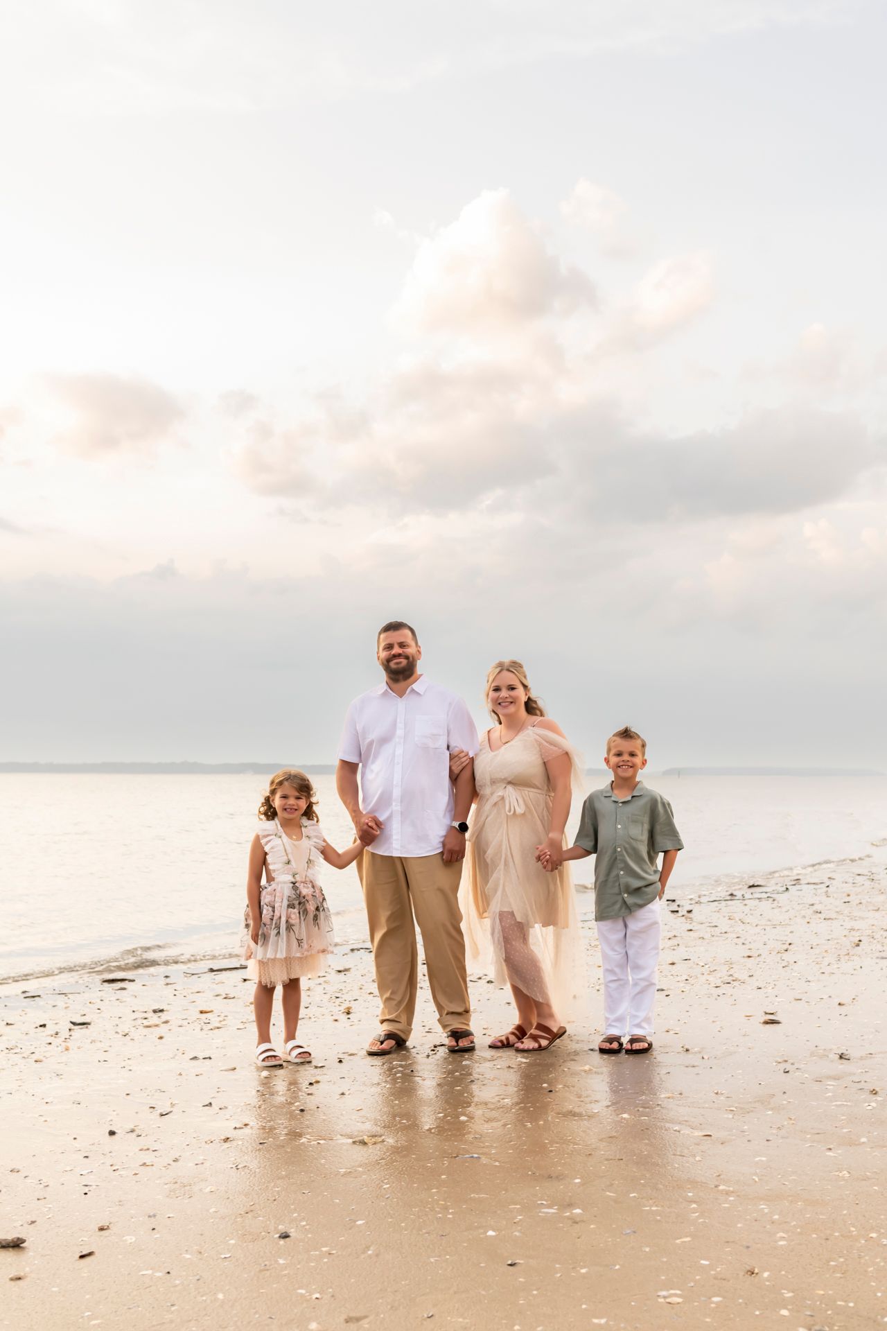 Family walking together on a white sandy beach at sunset wearing coordinated neutral colored outfits.