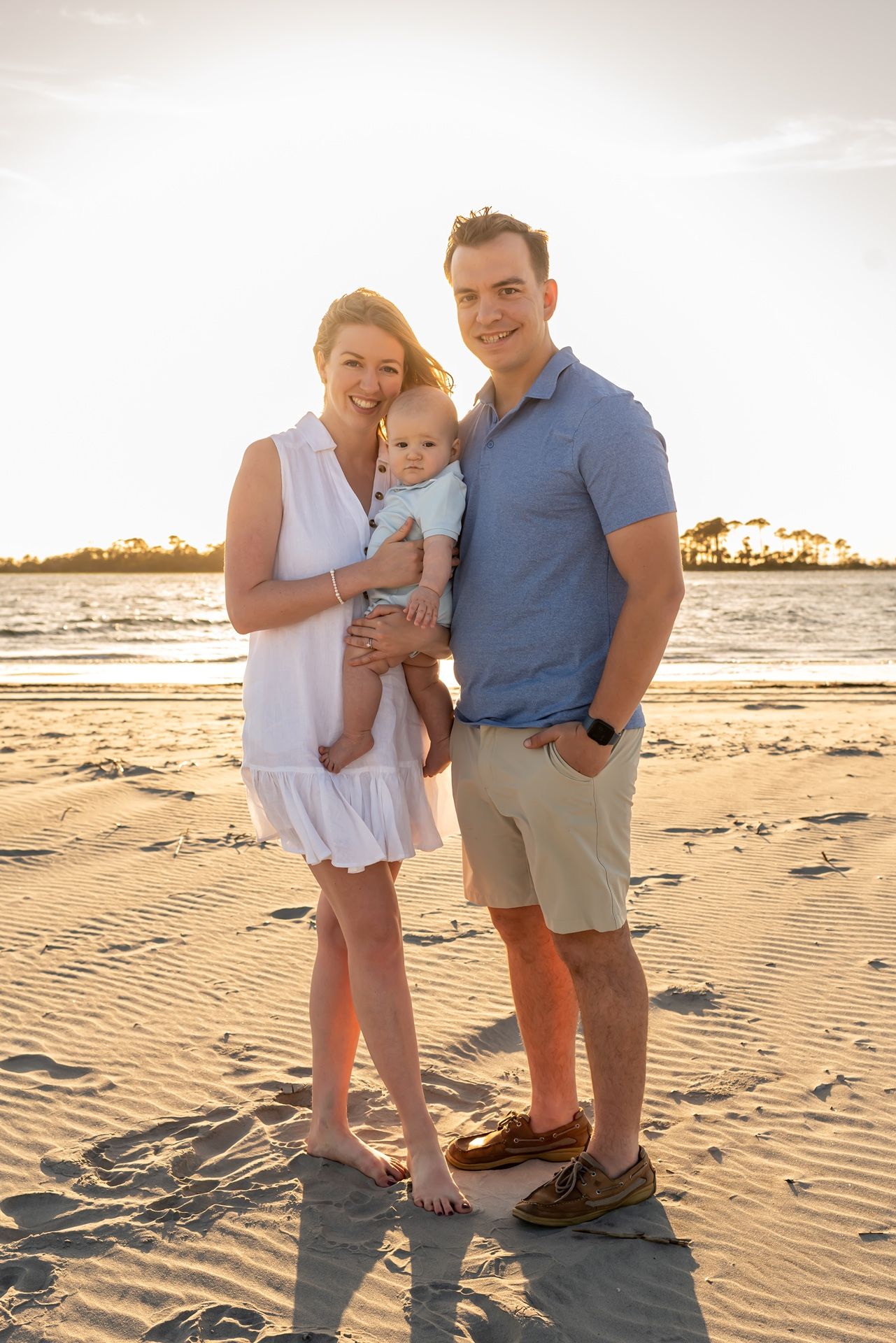A family stands together on a sandy beach at sunset with palm trees silhouetted in the golden background.