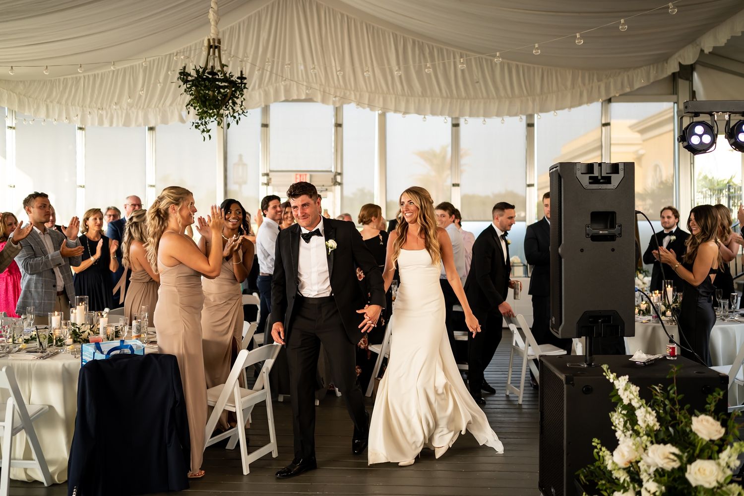 A newlywed couple dances together in a white reception tent filled with guests and white decor.