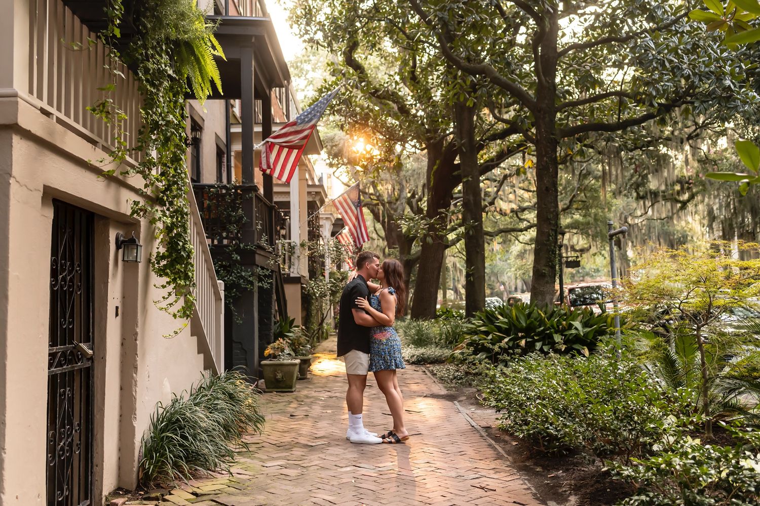 Two people embrace on a charming brick sidewalk in historic Charleston as sunlight filters through moss-draped trees.