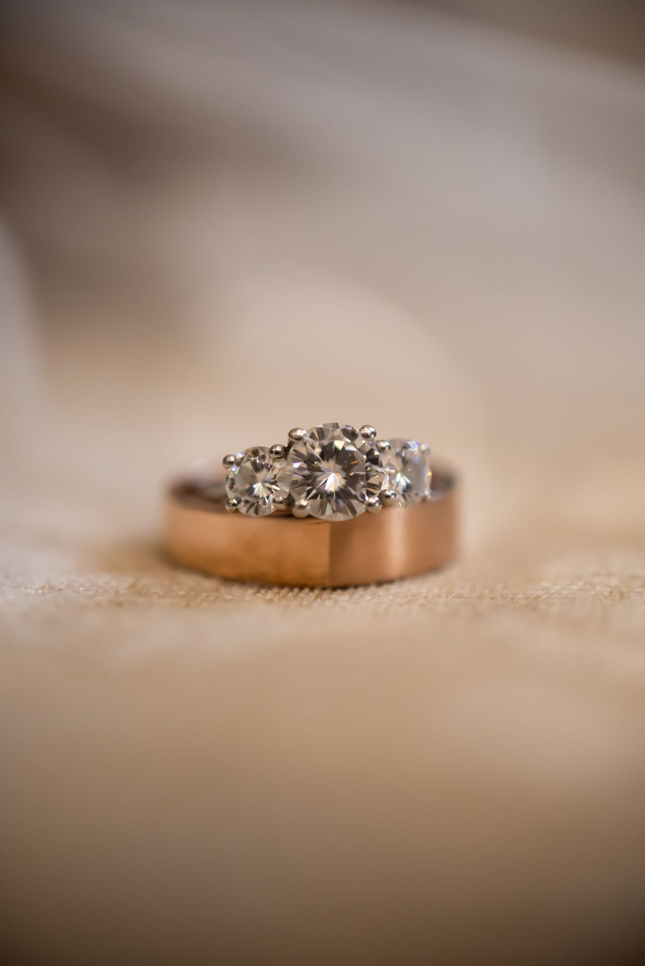A set of wedding rings with diamonds arranged on a beige textured surface with shallow depth of field.