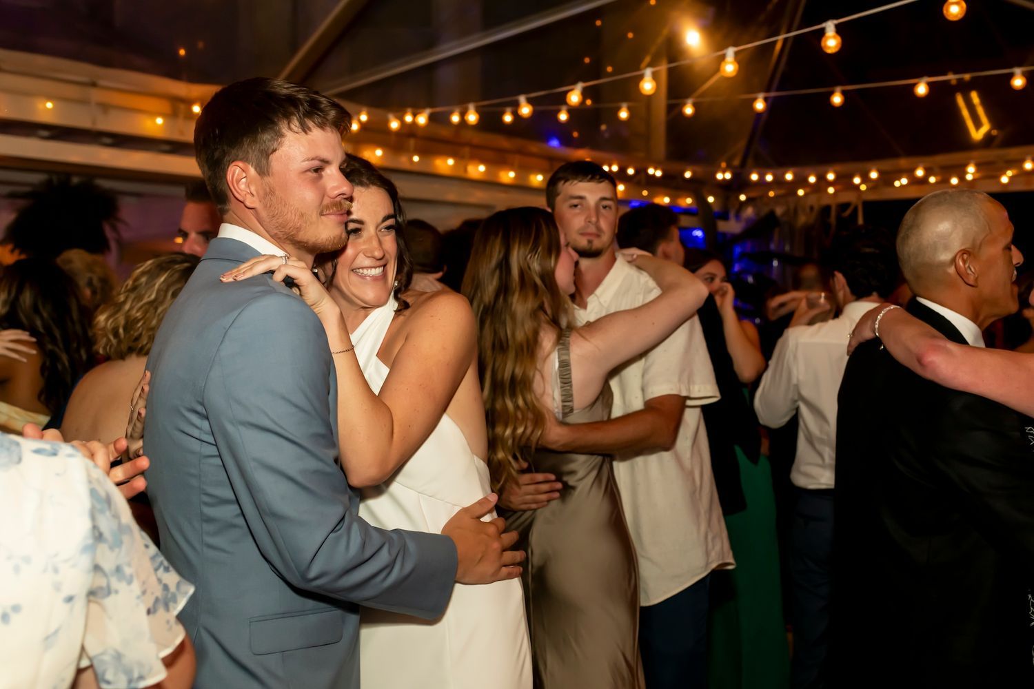 Couples dancing together under string lights at an evening wedding reception celebration.