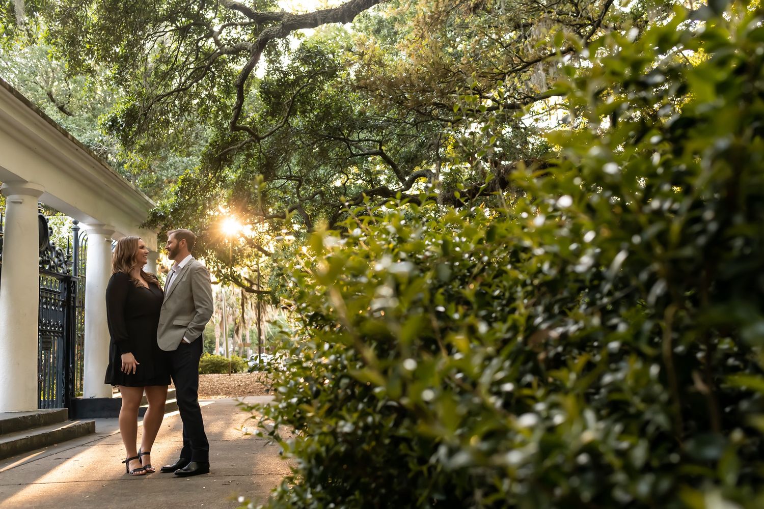 Couple walks together on a garden path with sunlight streaming through tree branches above.