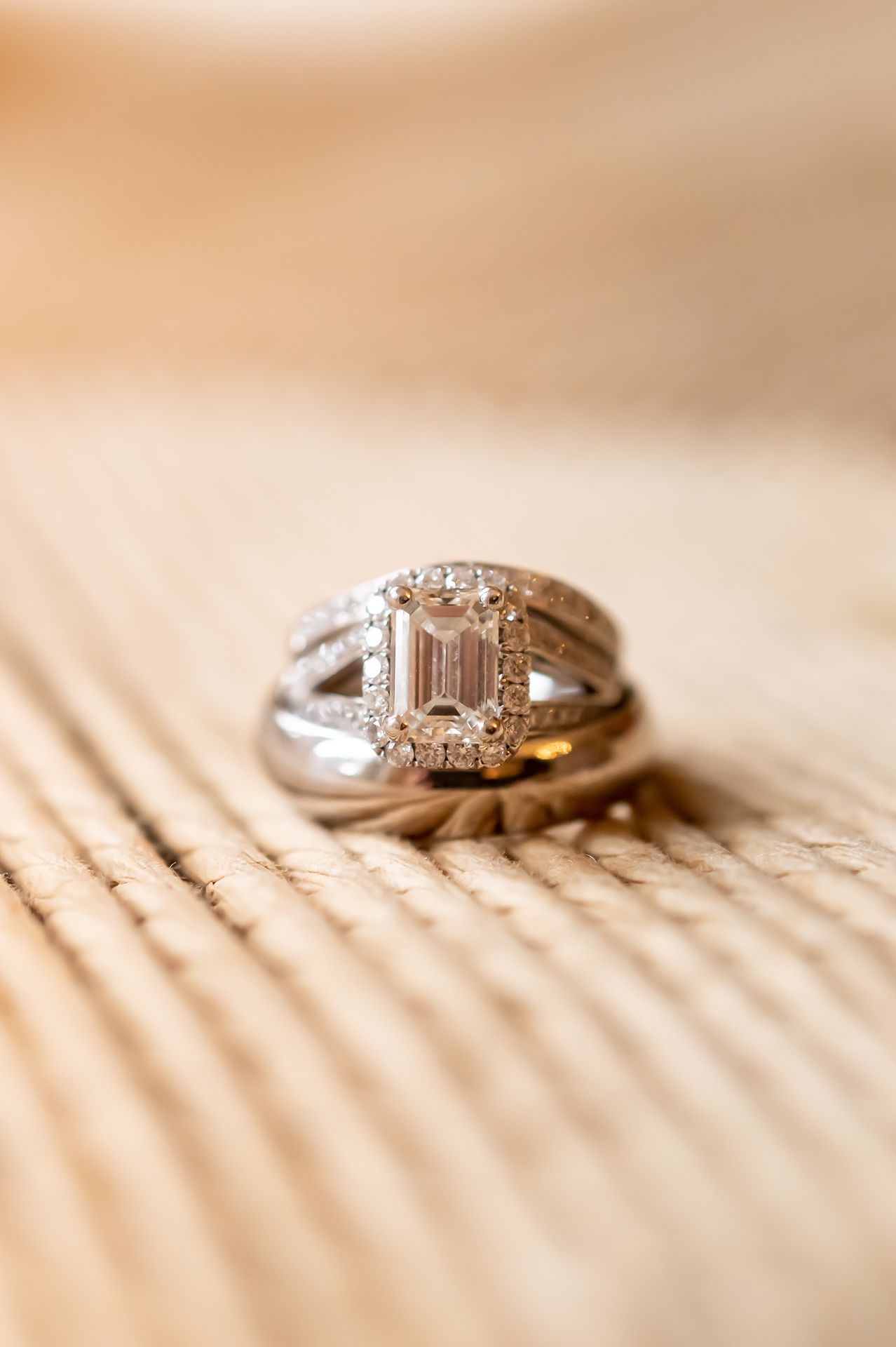 A diamond engagement ring with an emerald cut center stone and halo setting rests on a wooden surface.