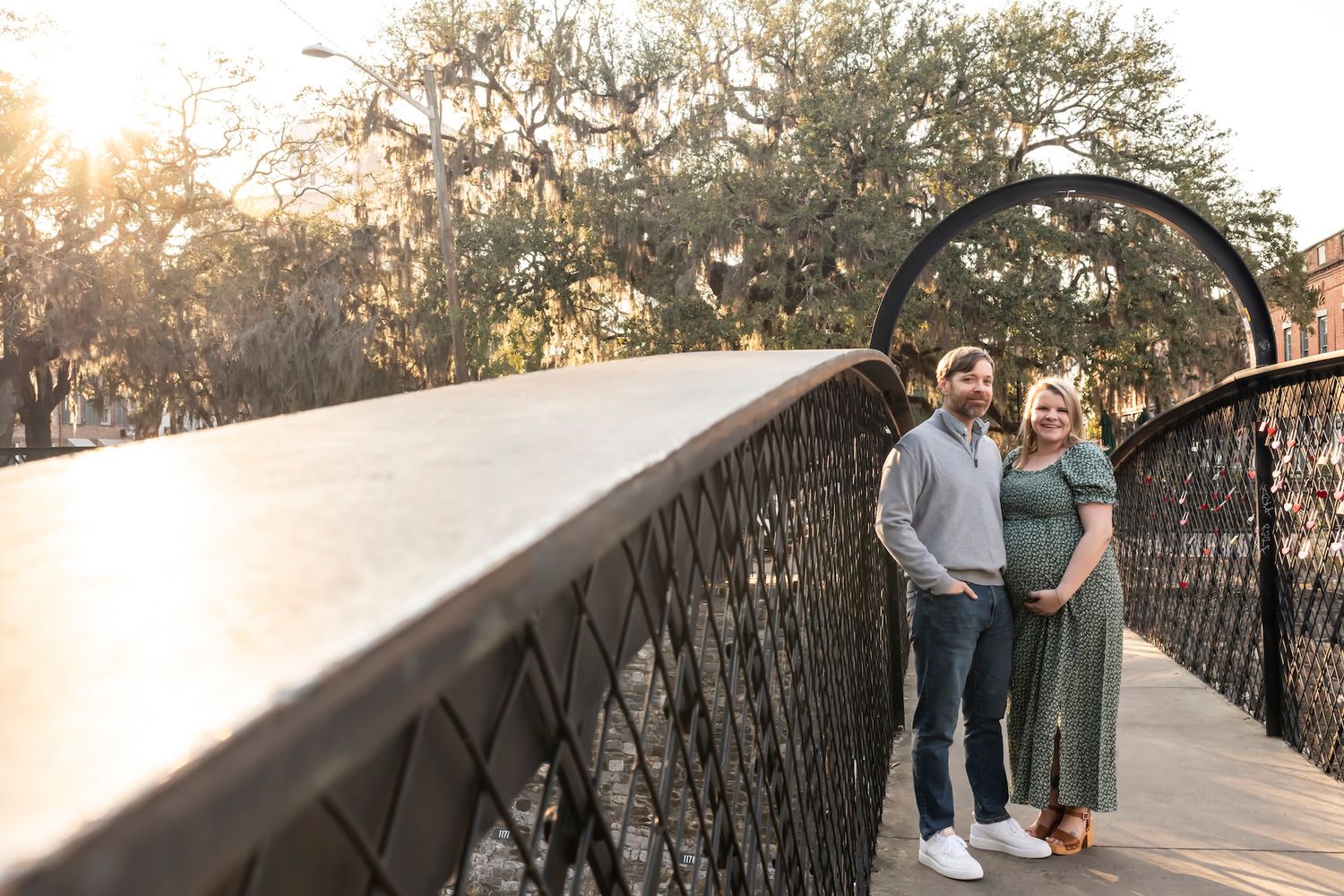 A couple walks along an illuminated bridge pathway at sunset while trees cast golden light through the branches.