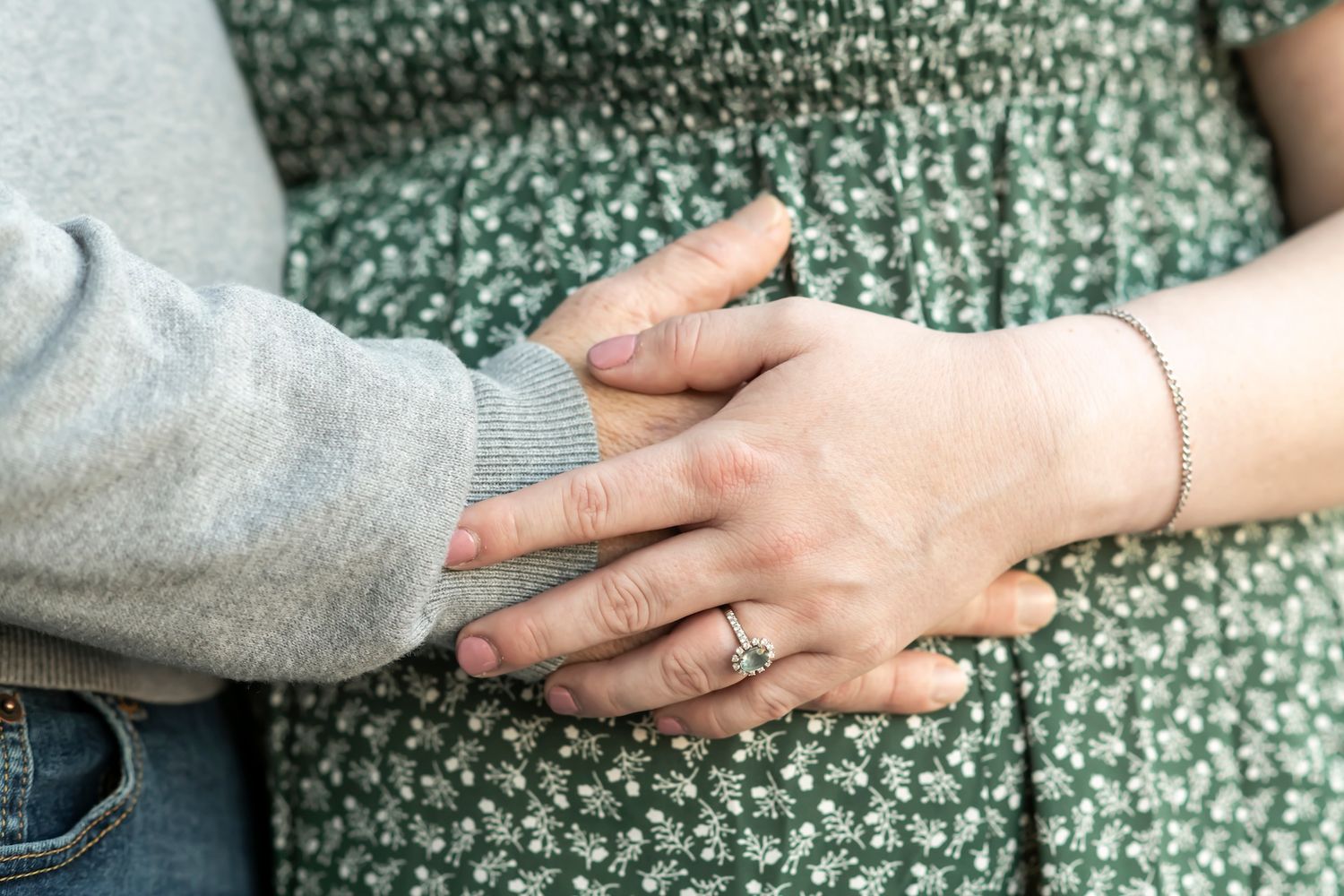 Close up of hands touching a pregnant belly against a green floral dress background.