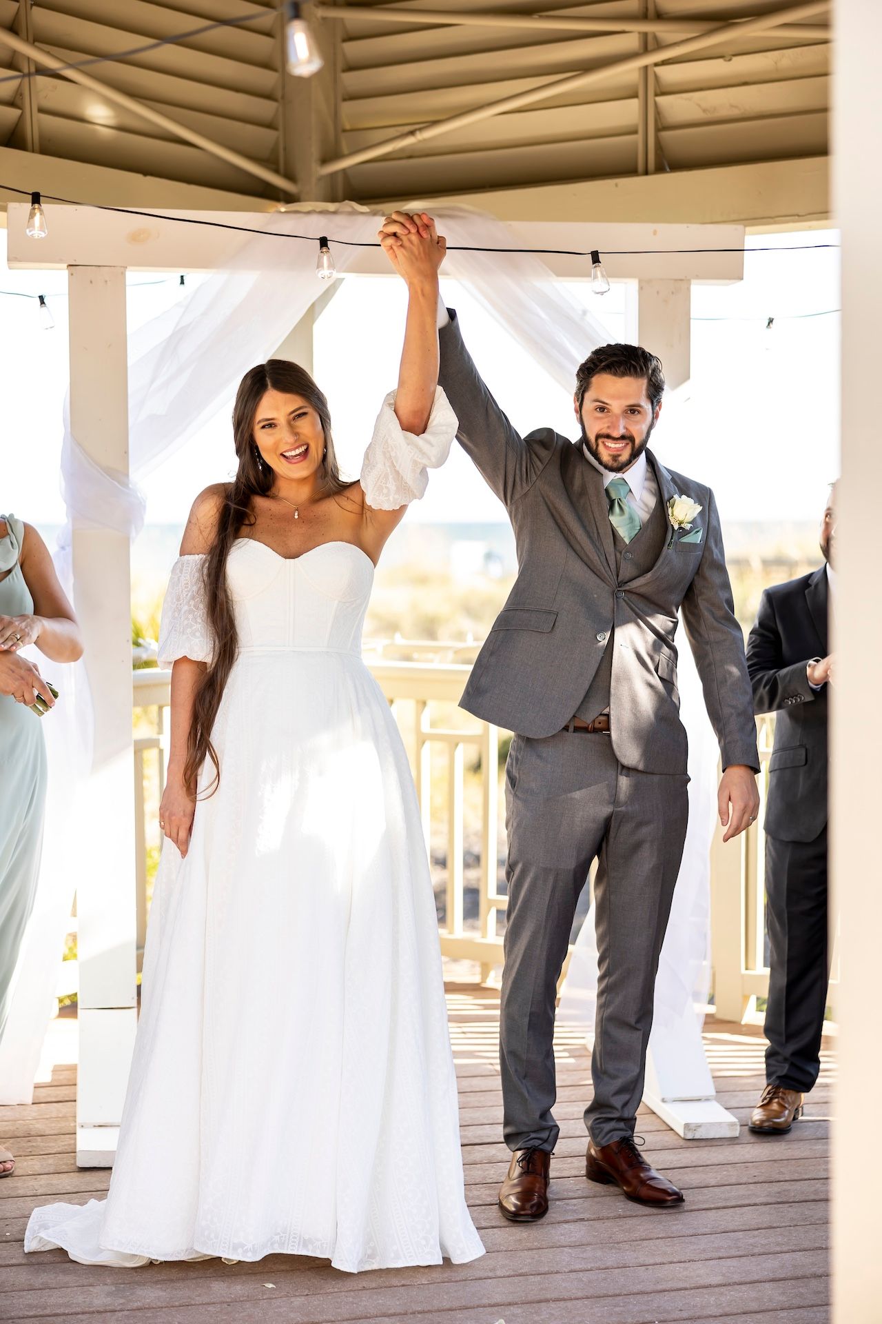 A joyful couple celebrates their marriage ceremony in an elegant white gazebo on a sunny day.