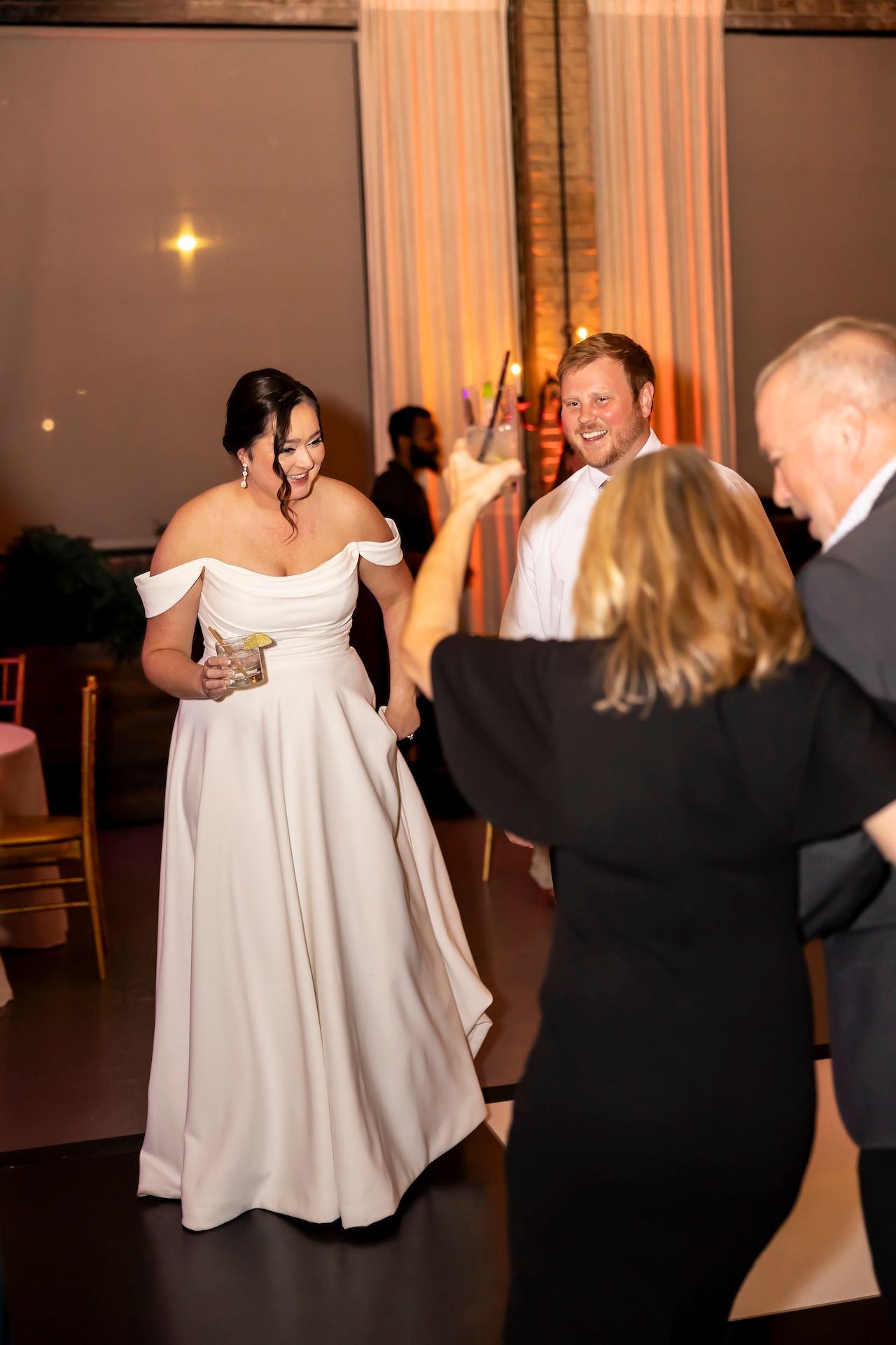 A bride in an off-shoulder white gown mingles with guests during the wedding reception.