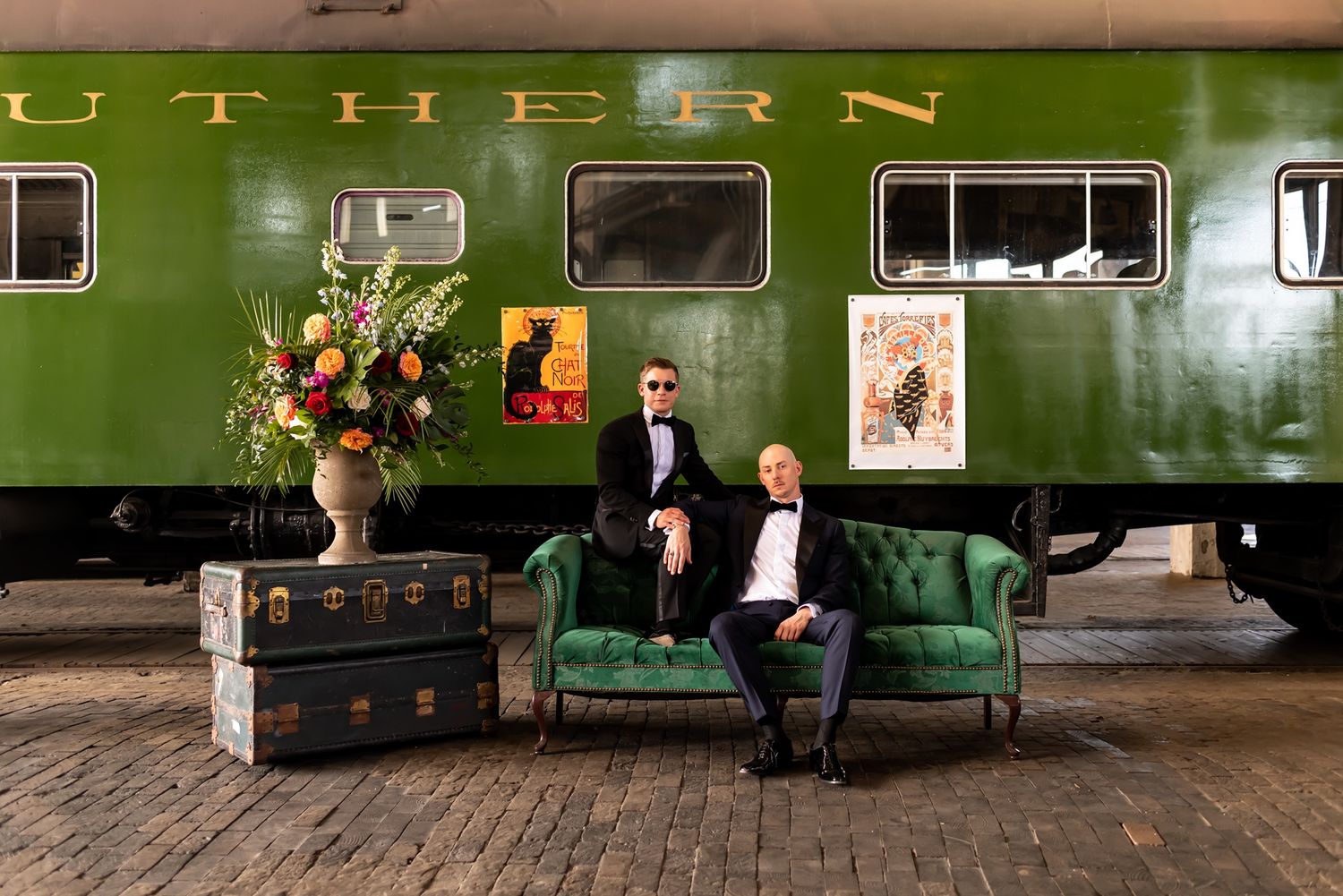 Panoramic view of an elegant vintage interior with green velvet sofas, wooden floors, and artistic floral arrangements.
