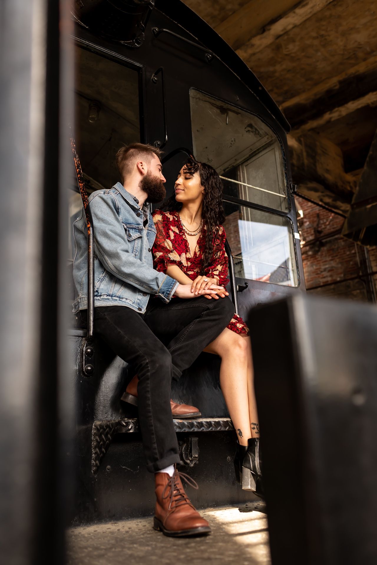 Stylish couple shares intimate moments in a rustic industrial setting with dramatic lighting and shadows.