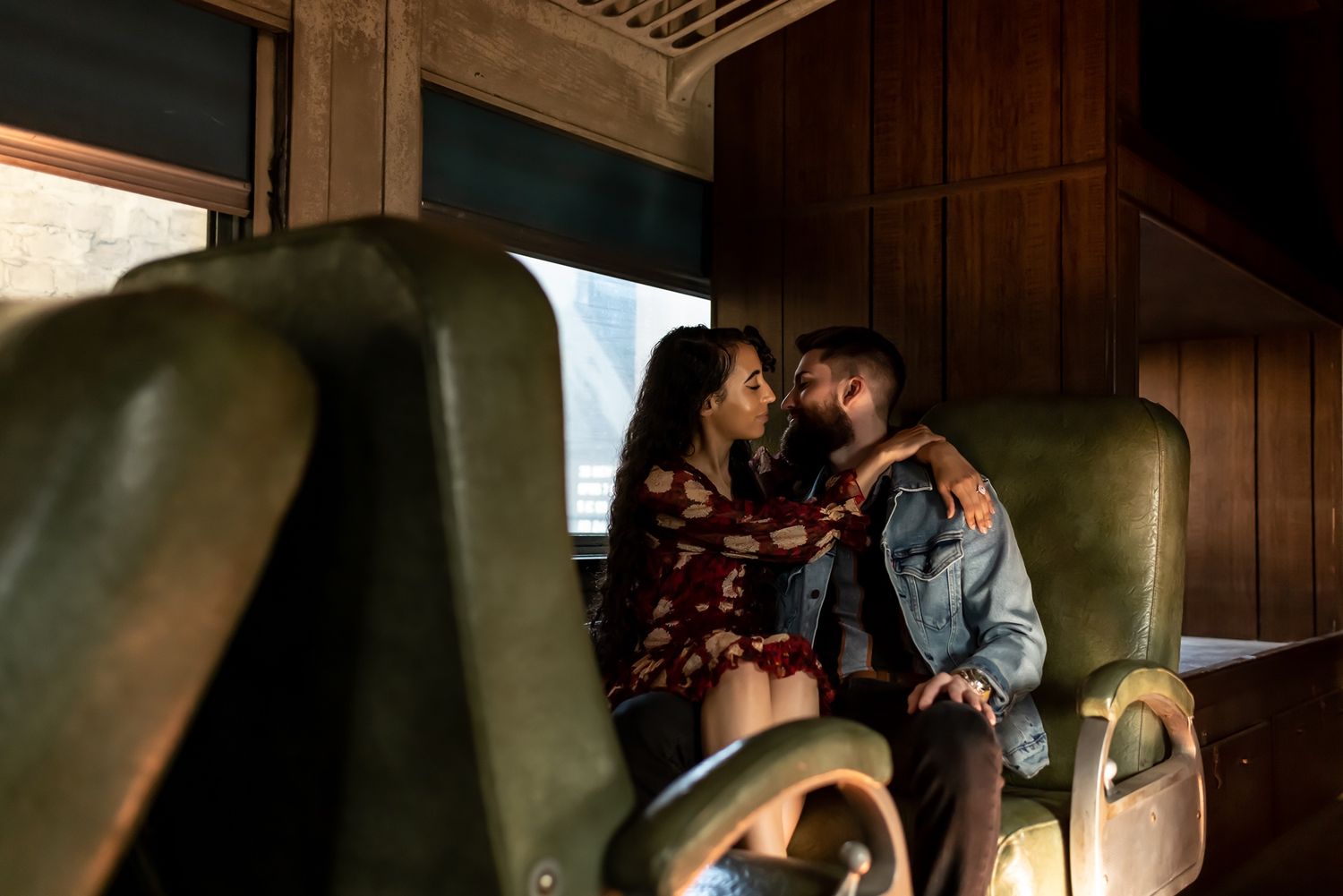 A couple shares an intimate moment inside a dimly lit room with wooden paneled walls.