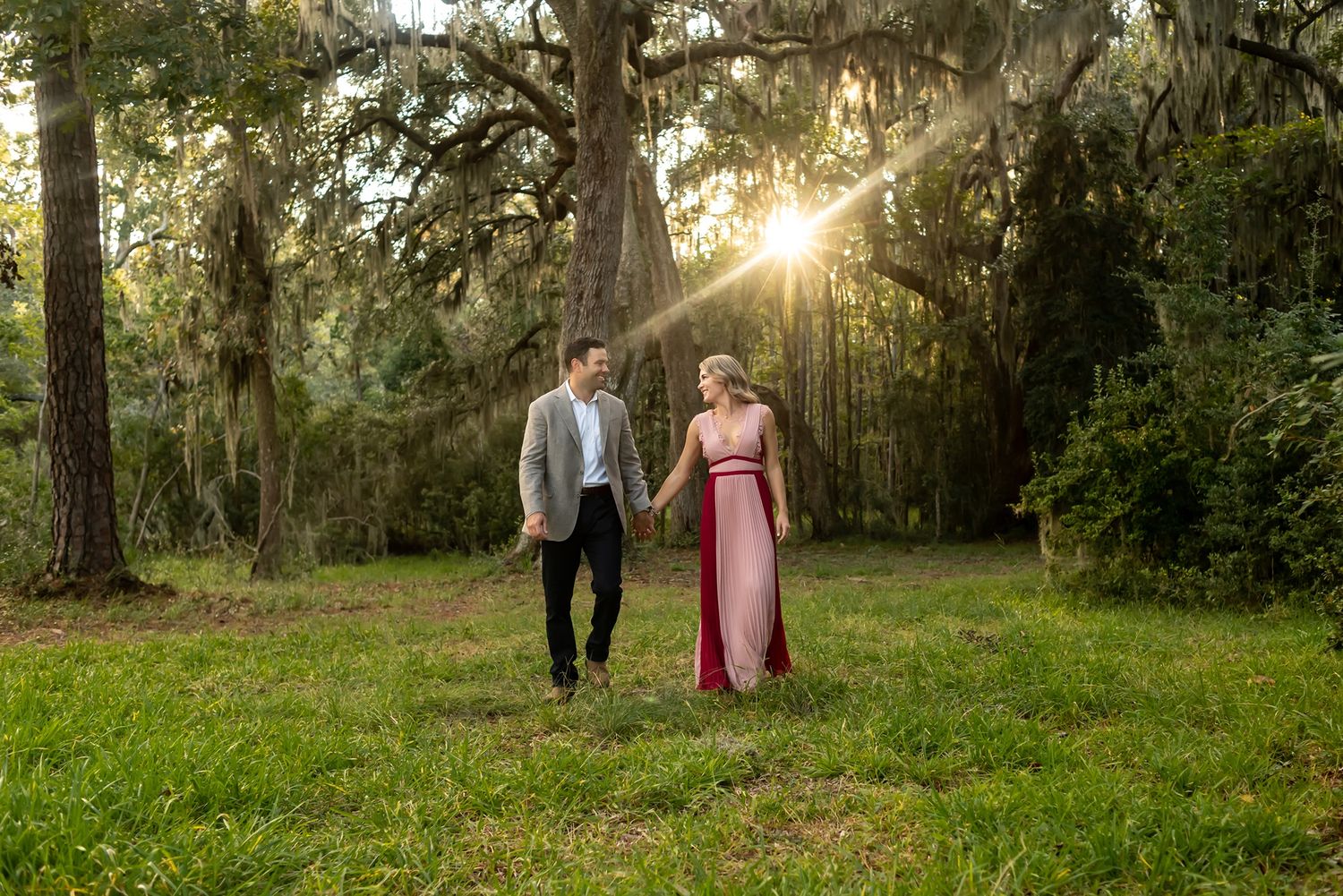 Couple walking through a sun-dappled park with Spanish moss hanging from trees during golden hour.