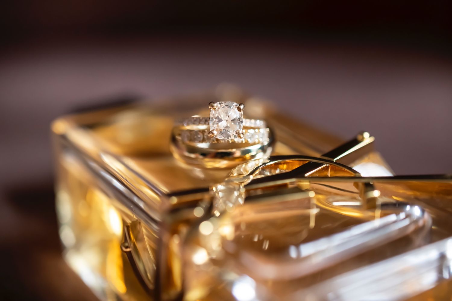 Close-up macro photography of gold wedding rings with diamonds displayed on reflective surfaces in warm lighting.
