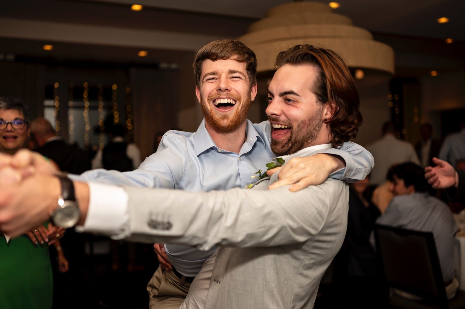 Two guests laugh joyfully and embrace while dancing at an indoor celebration event.