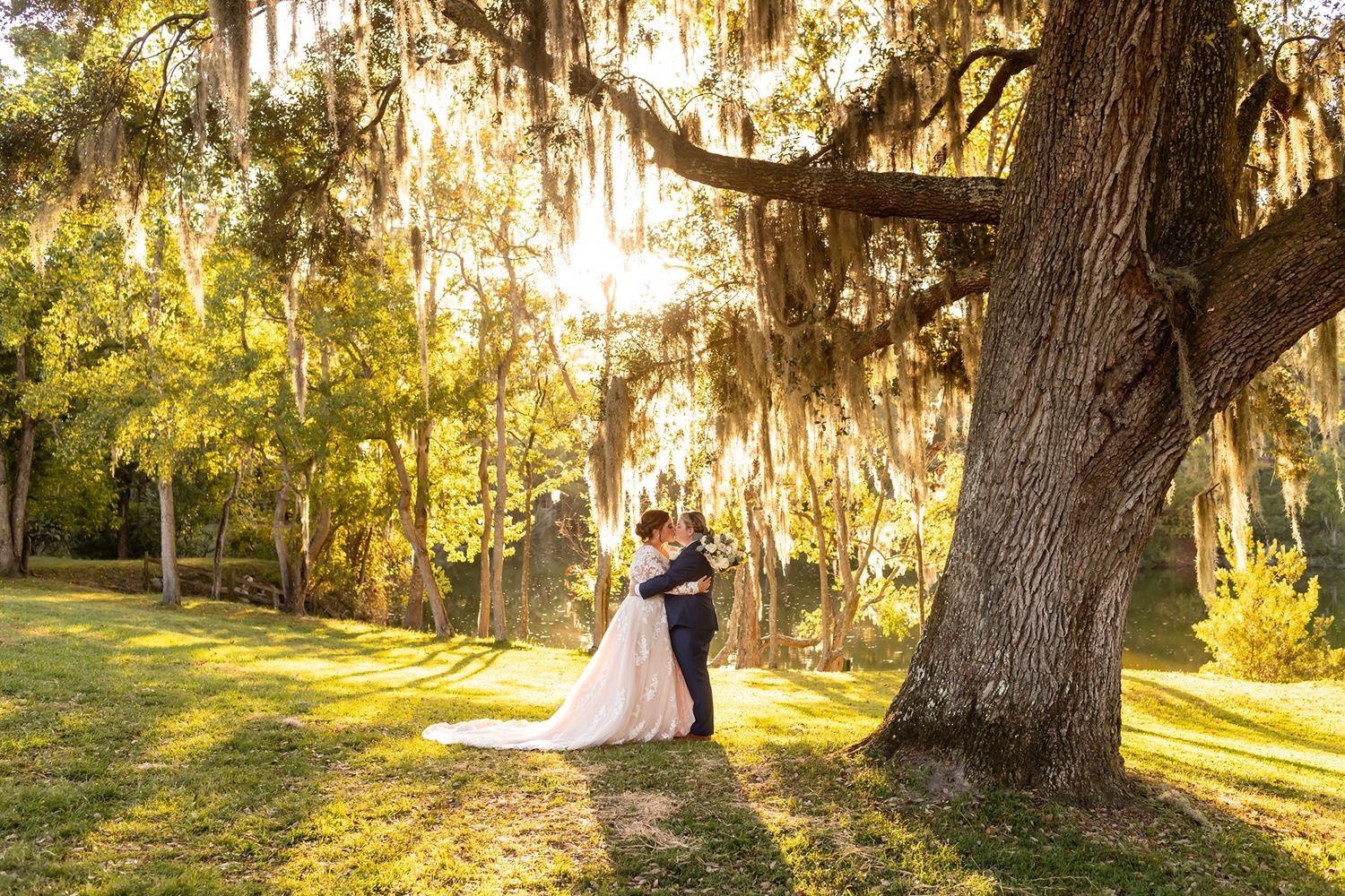 A couple embraces under majestic Spanish moss-draped oak trees at sunset in a romantic garden setting.
