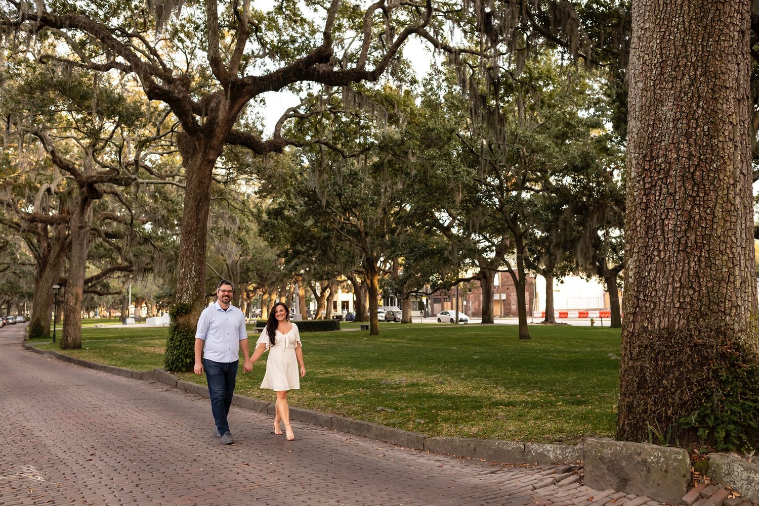 Couple walks together along a scenic tree-lined path in a historic park with Spanish moss hanging from live oaks.
