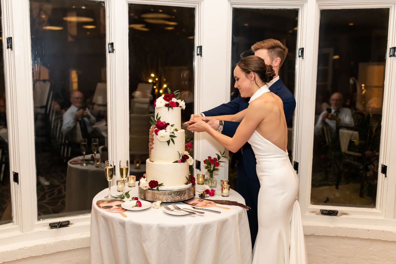 Newlyweds share a romantic moment on a glass-enclosed veranda decorated with pink roses during their wedding reception.