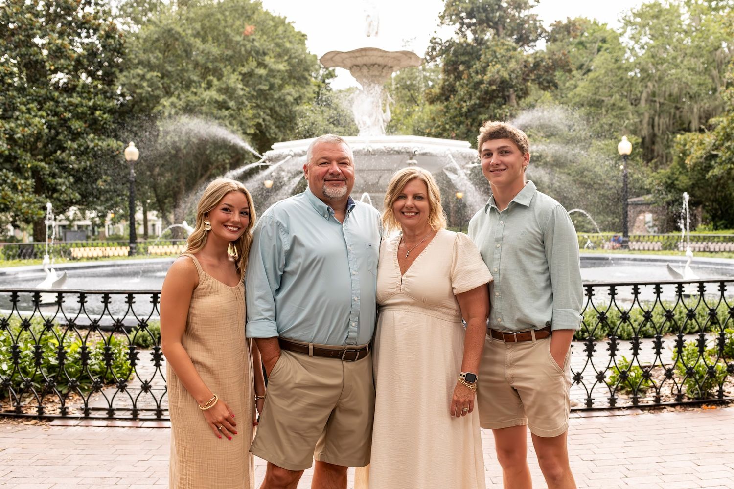 Group stands together smiling in front of a fountain at a scenic park on a sunny summer day.