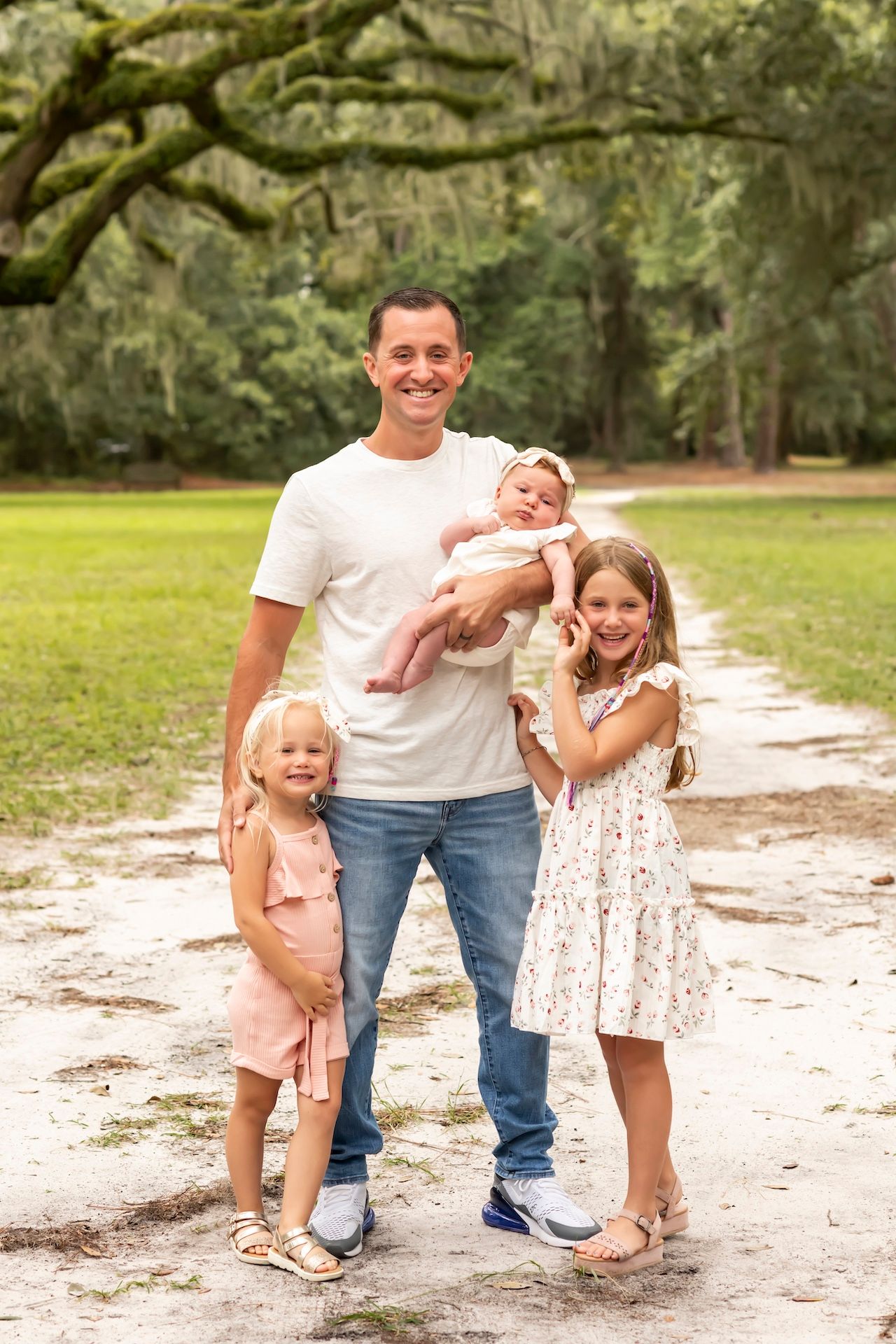 Family enjoying a playful moment together on a sandy path surrounded by green trees in an outdoor setting.