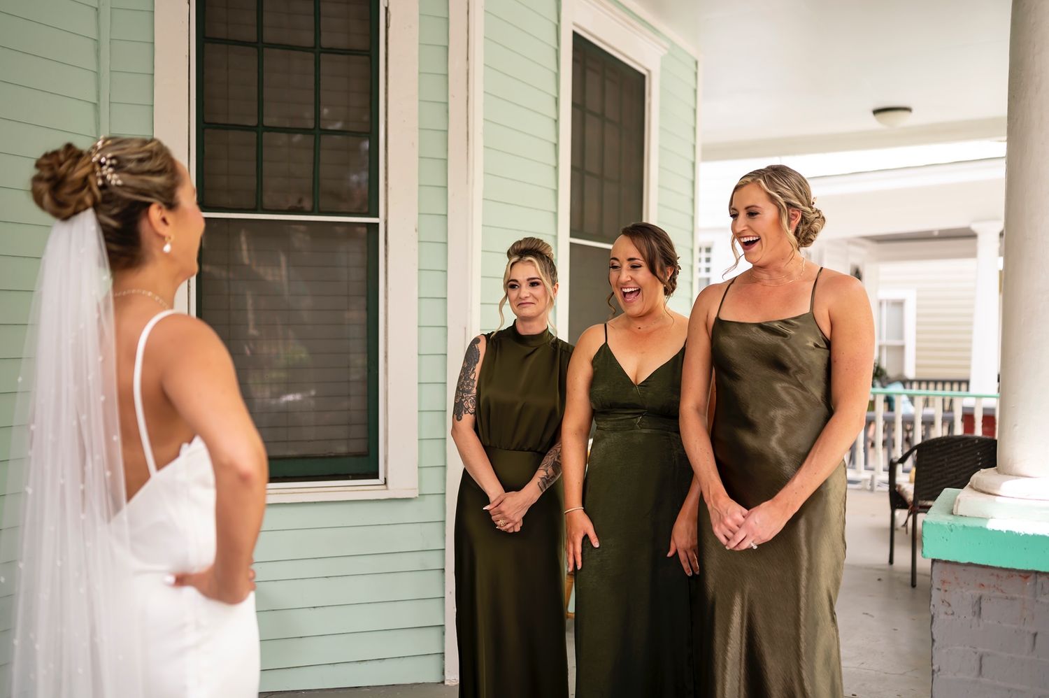 A wedding party stands in a row wearing black attire with sage green walls in the background.