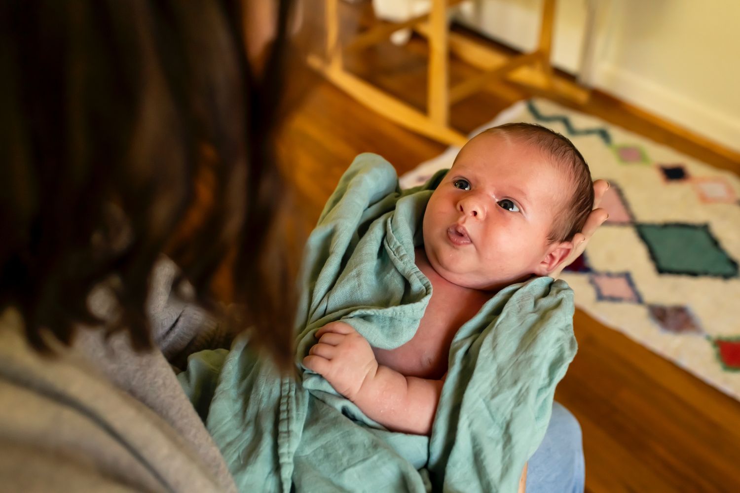 A small infant wrapped in a mint green towel looks up with alert eyes during bath time.