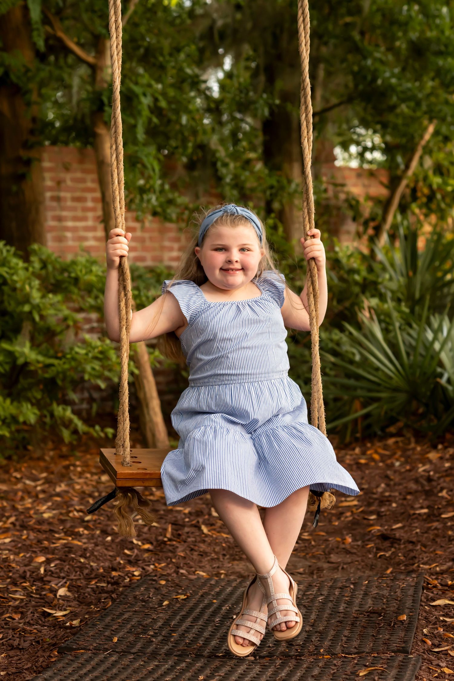 A progression series showing a child in a light blue dress sitting and smiling on a rope swing in a garden setting.