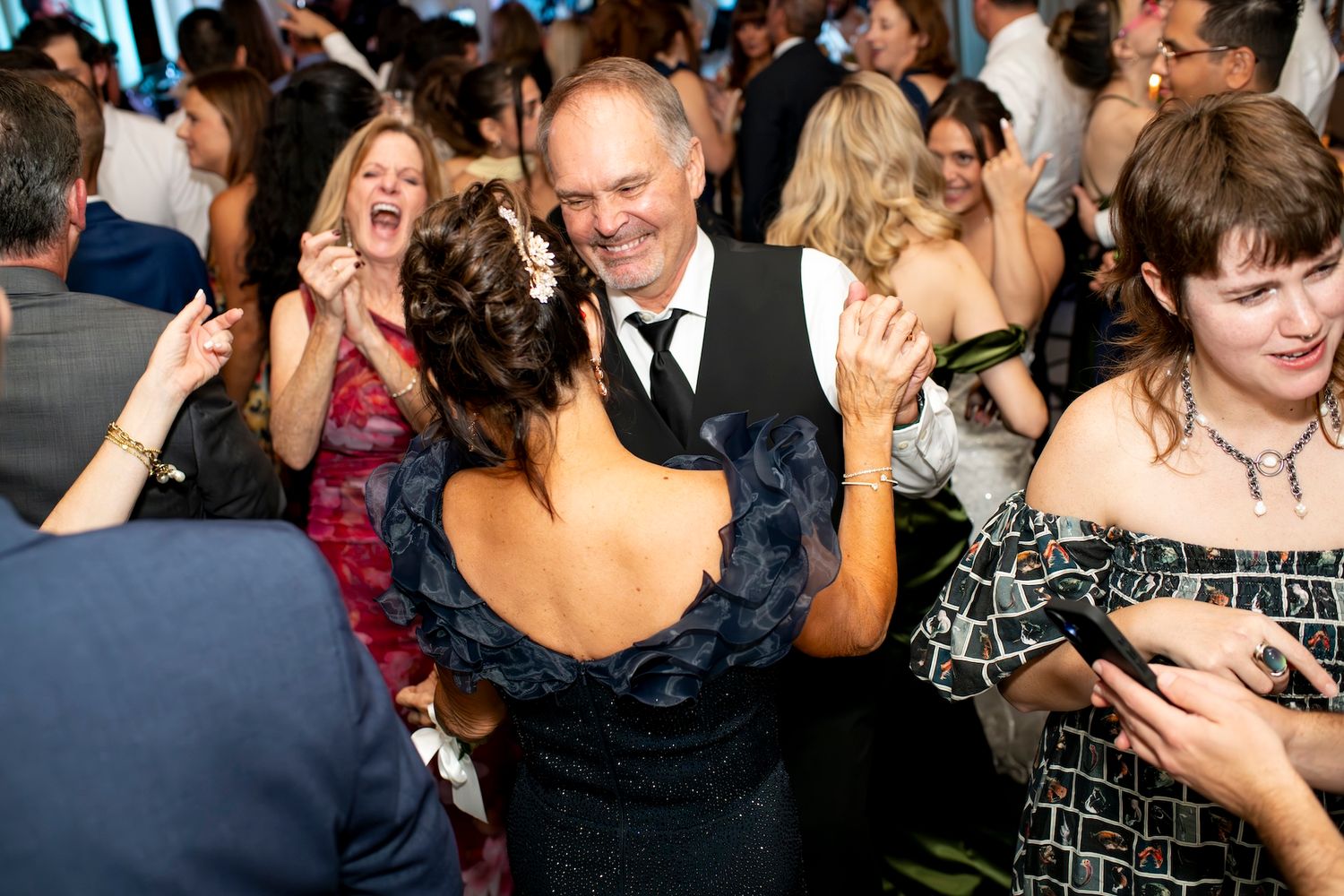 Energetic crowd of wedding guests dancing and celebrating together on a dark dance floor at a reception party.