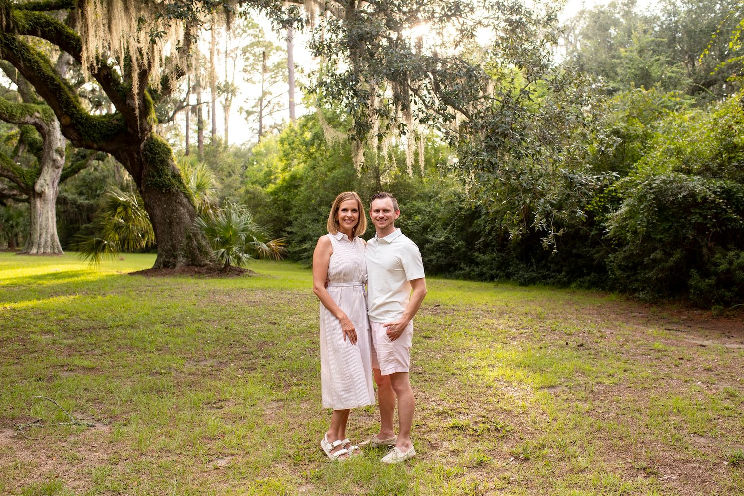 Couple smiling together under a large oak tree with Spanish moss in a lush green park setting.