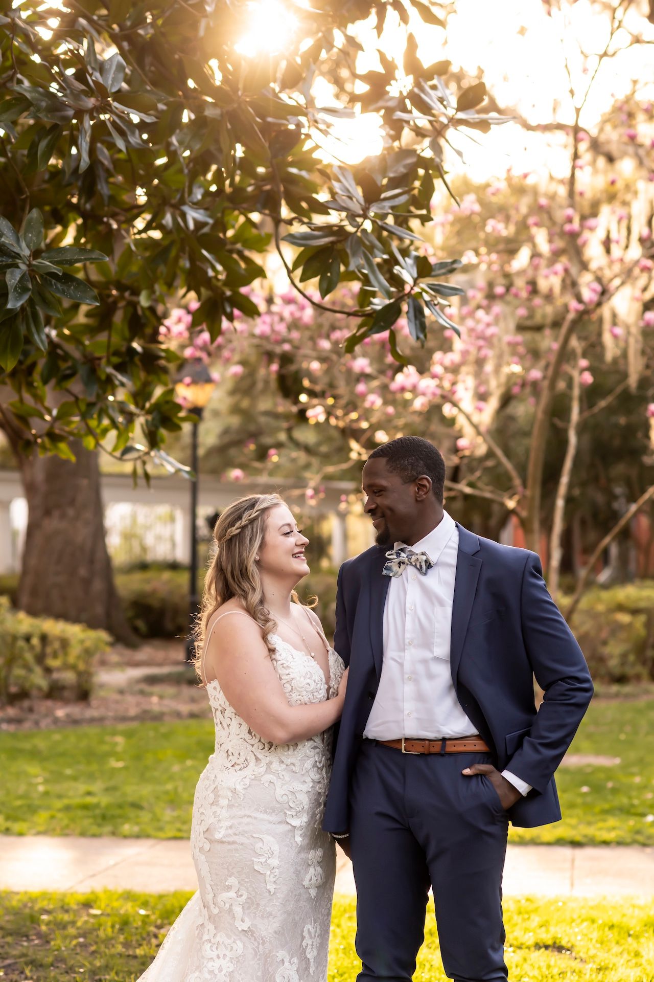 A couple shares a joyful moment under blooming trees at sunset in Forsyth Park.