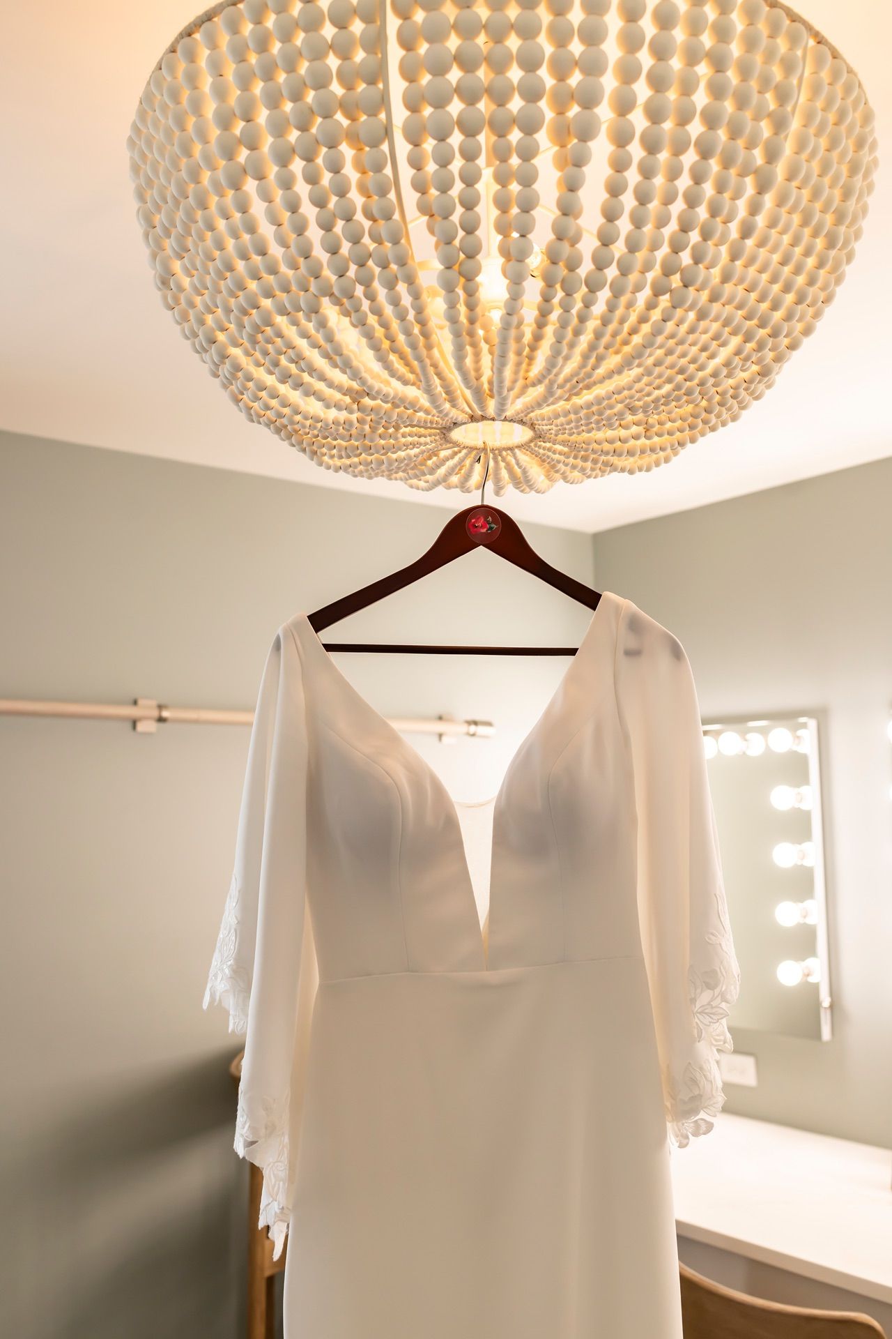 Elegant white wedding dress hanging beneath a crystal beaded dome chandelier.