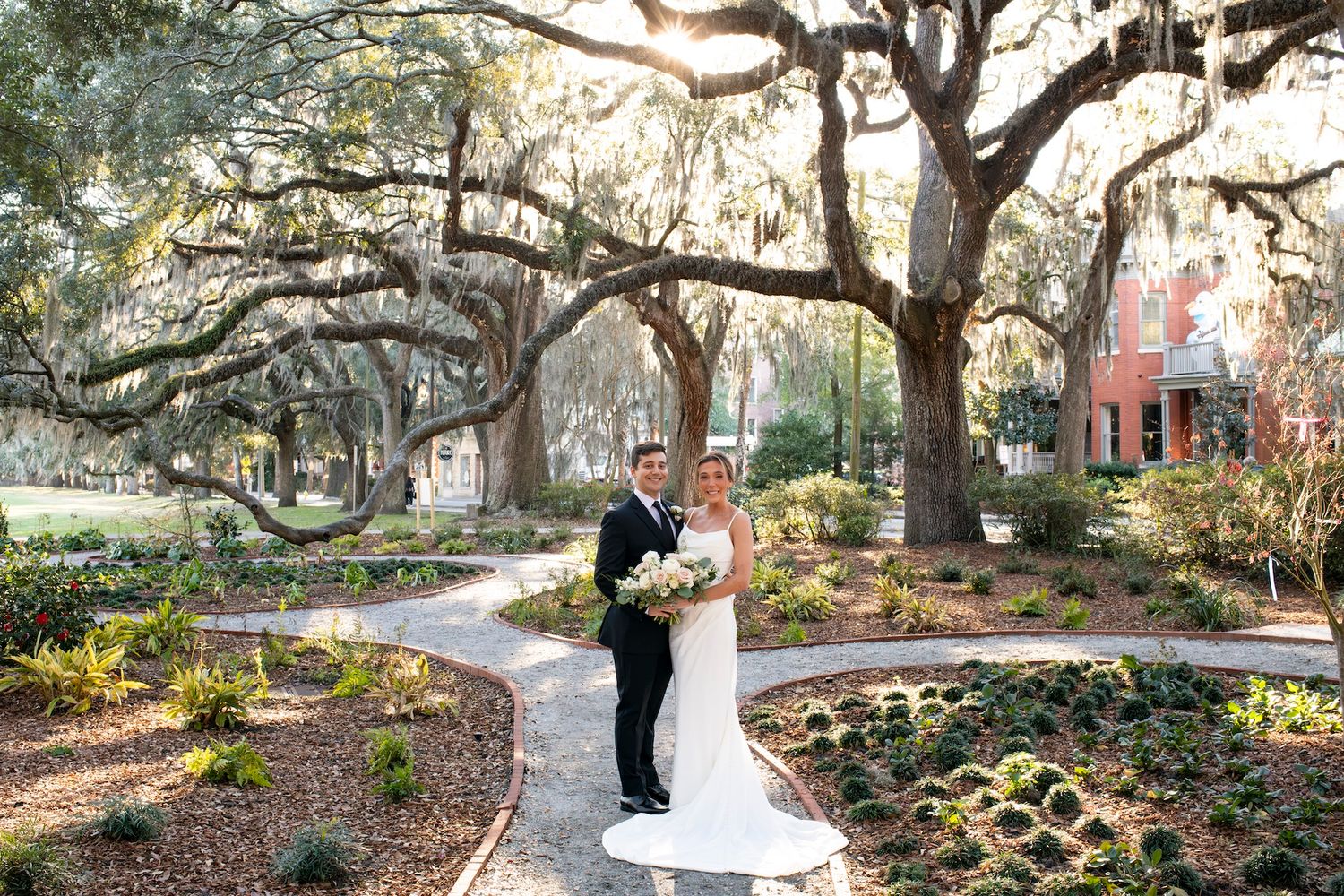 A bride and groom stand on a romantic path beneath majestic oak trees draped with Spanish moss in Forsyth Park.