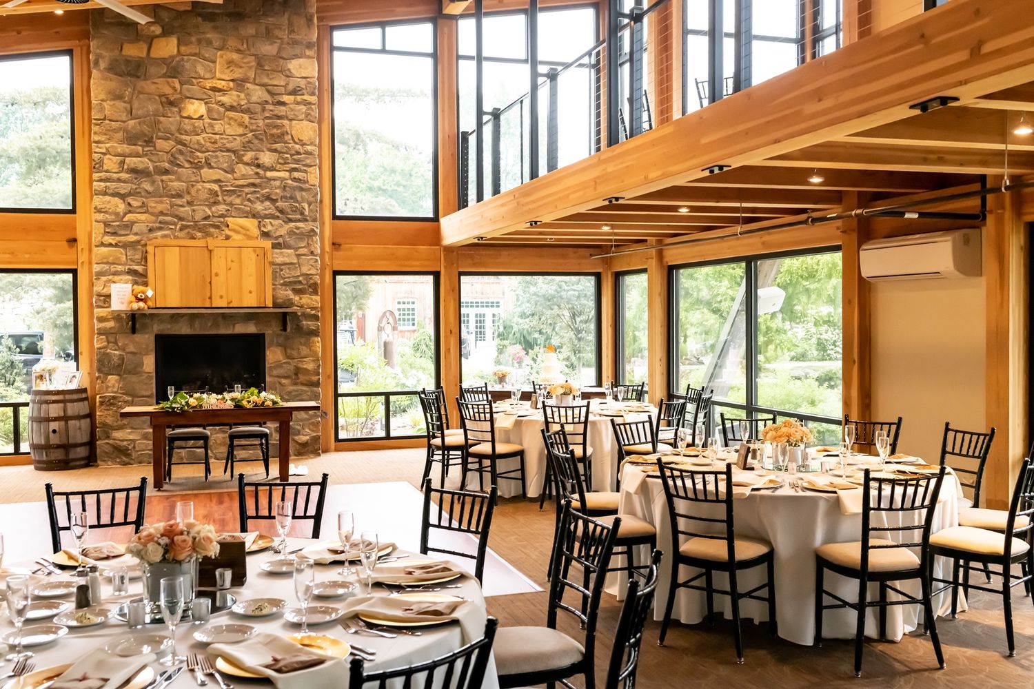 Elegant rustic dining room with stone fireplace, floor-to-ceiling windows, wooden beams and formal table settings.