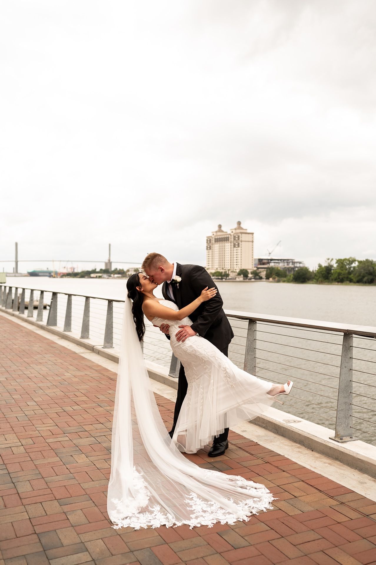 A loving couple in wedding attire share romantic dance poses on a waterfront brick terrace during their celebration.