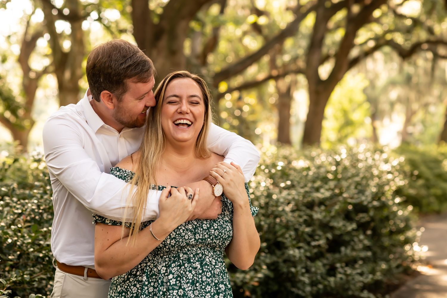 A couple shares joyful moments together on a shaded path surrounded by greenery and natural light.